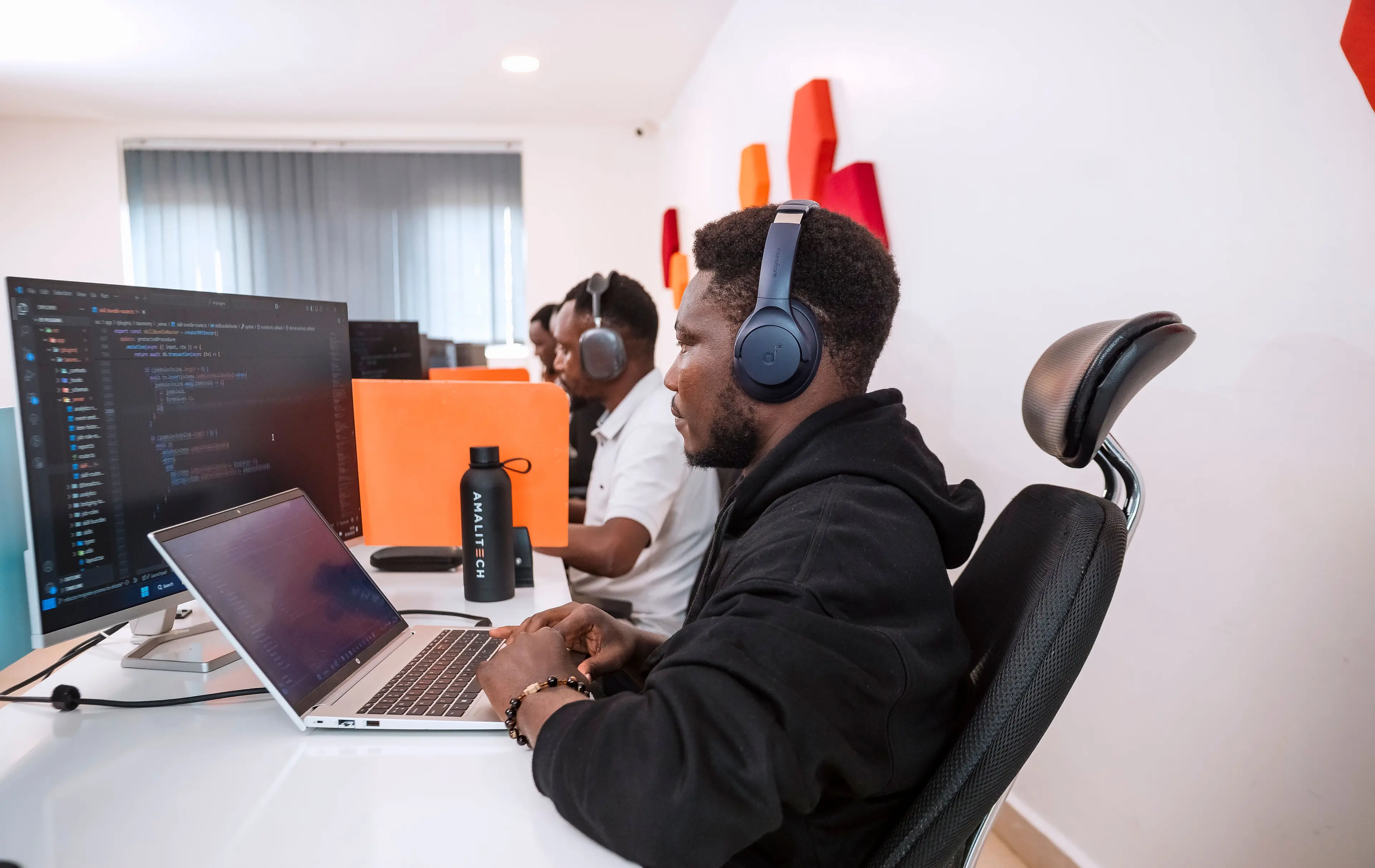 a man wearing headphone, working at his desk, using his laptop and additional big screen