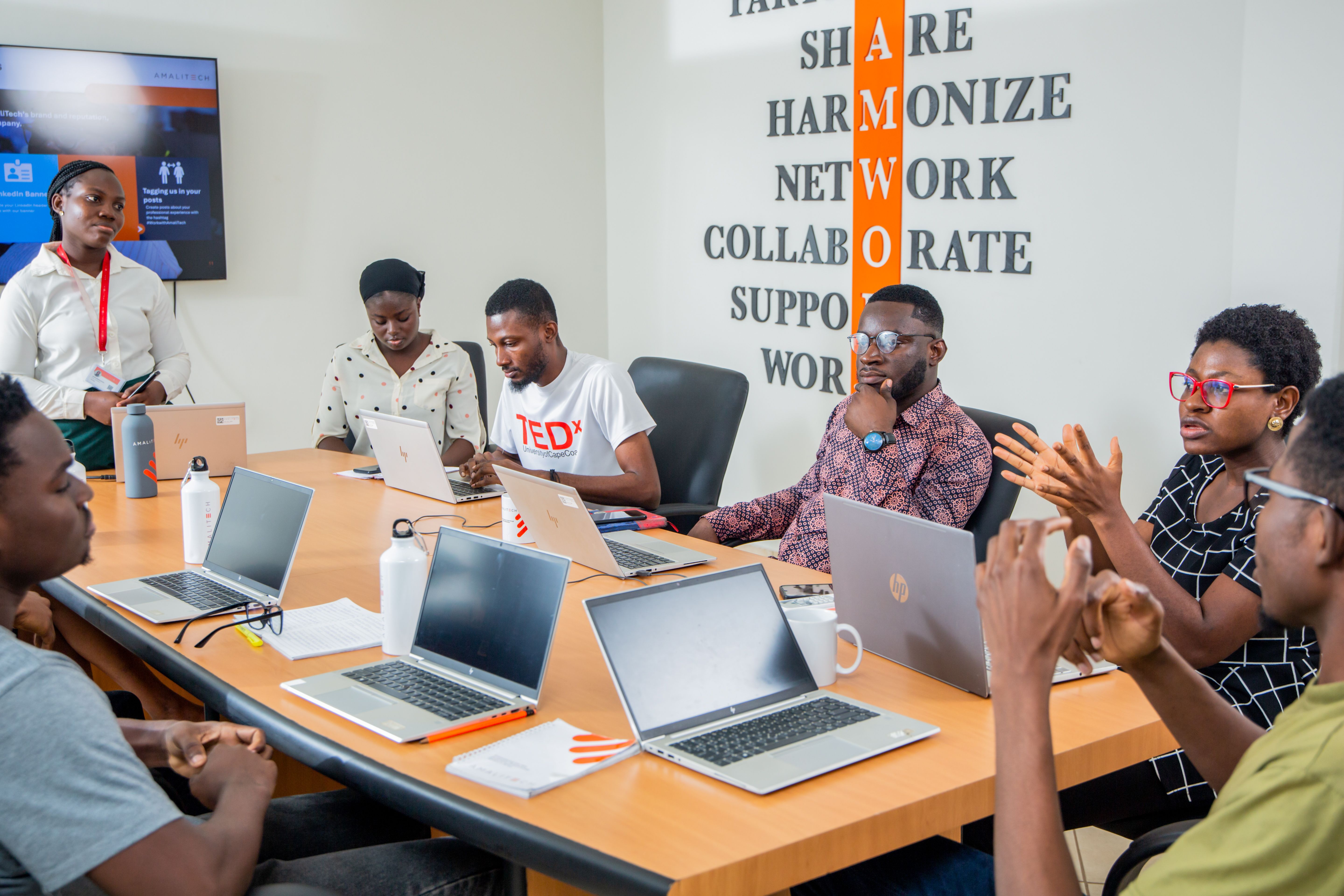 A group of people sitting in a conference room with laptops in front of them, discussing.