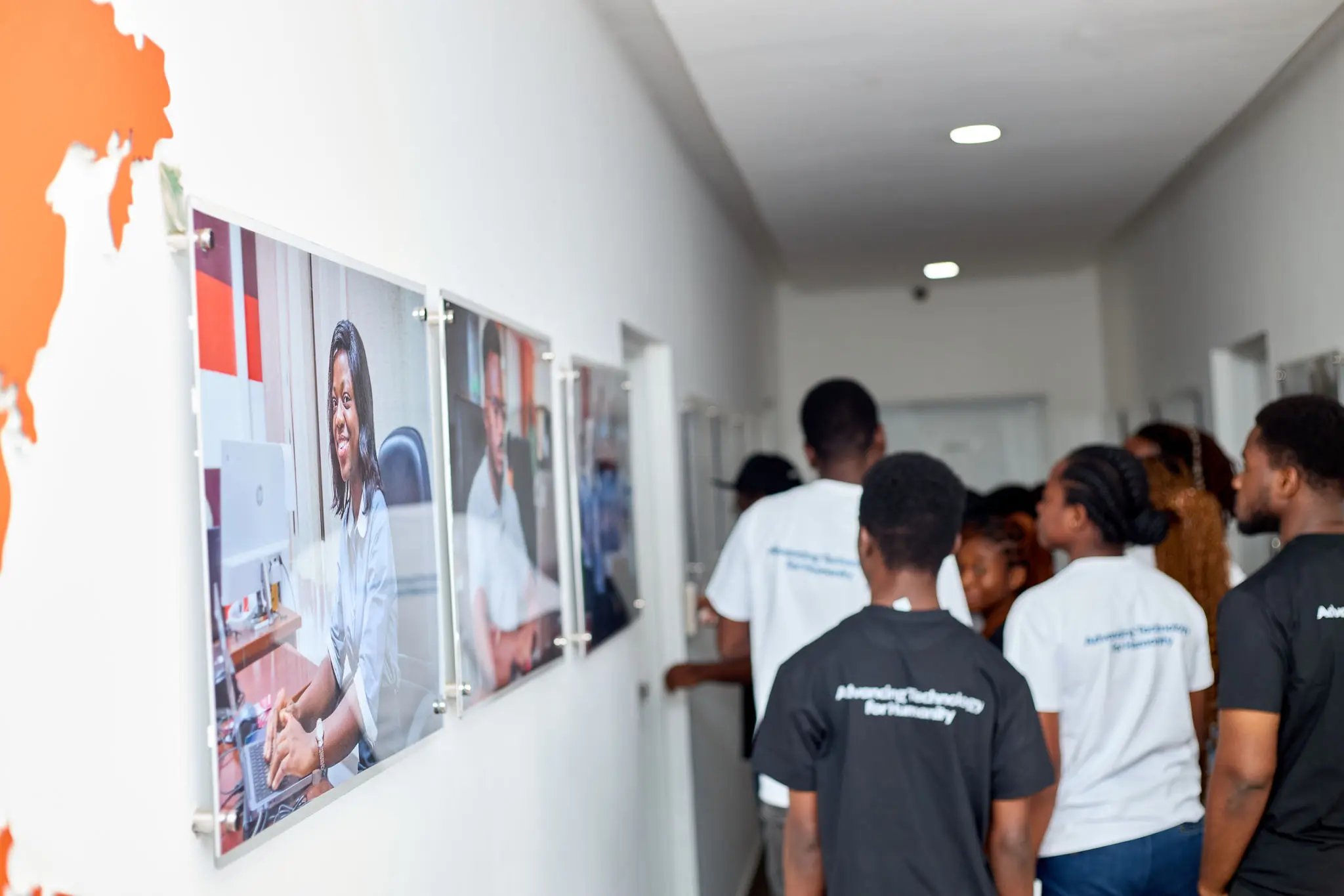 	IEEE KNUST students walk through an AmaliTech Kumasi corridor lined with framed photographs of team members at work.