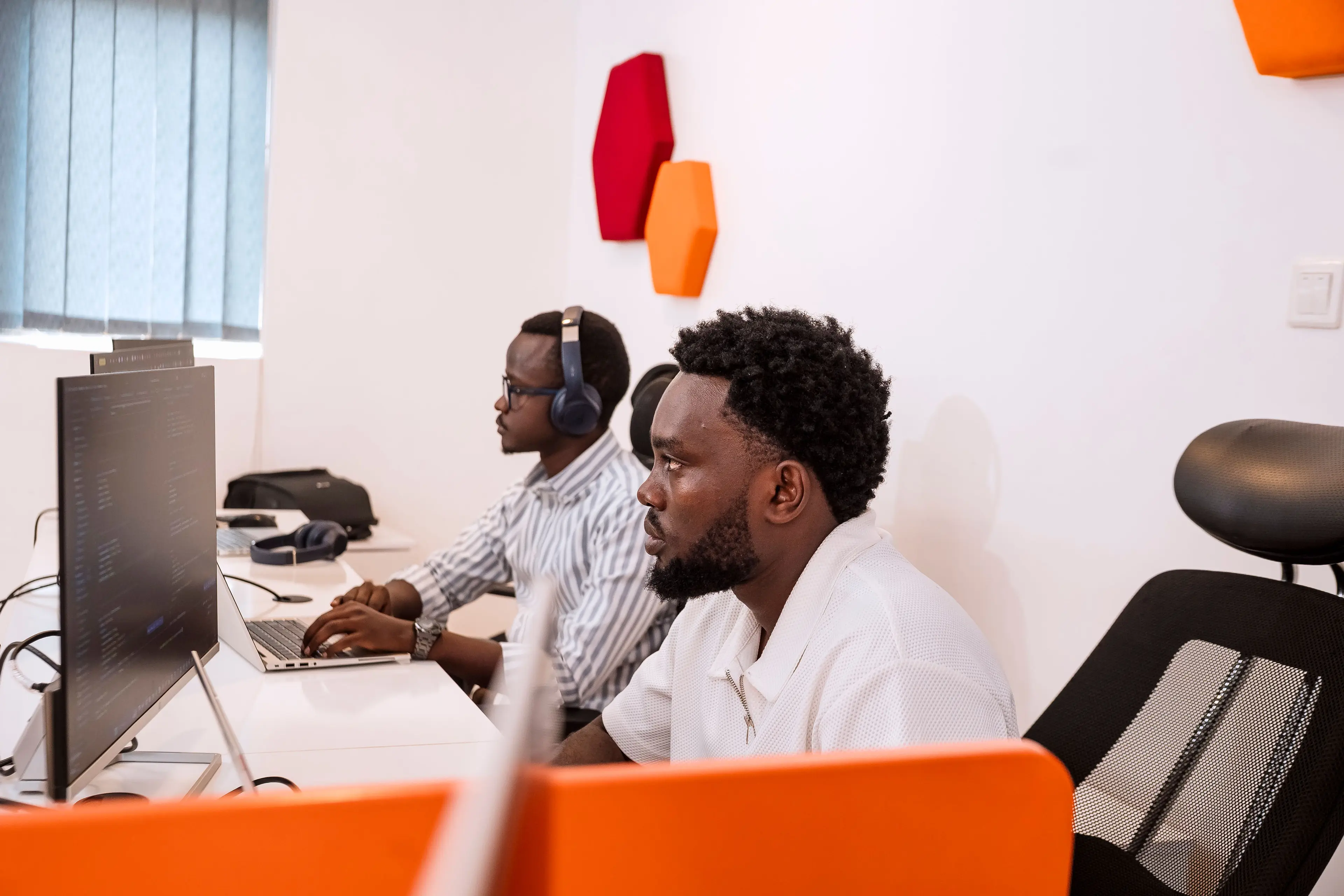 Two men working on their laptops, sitting at their desks.