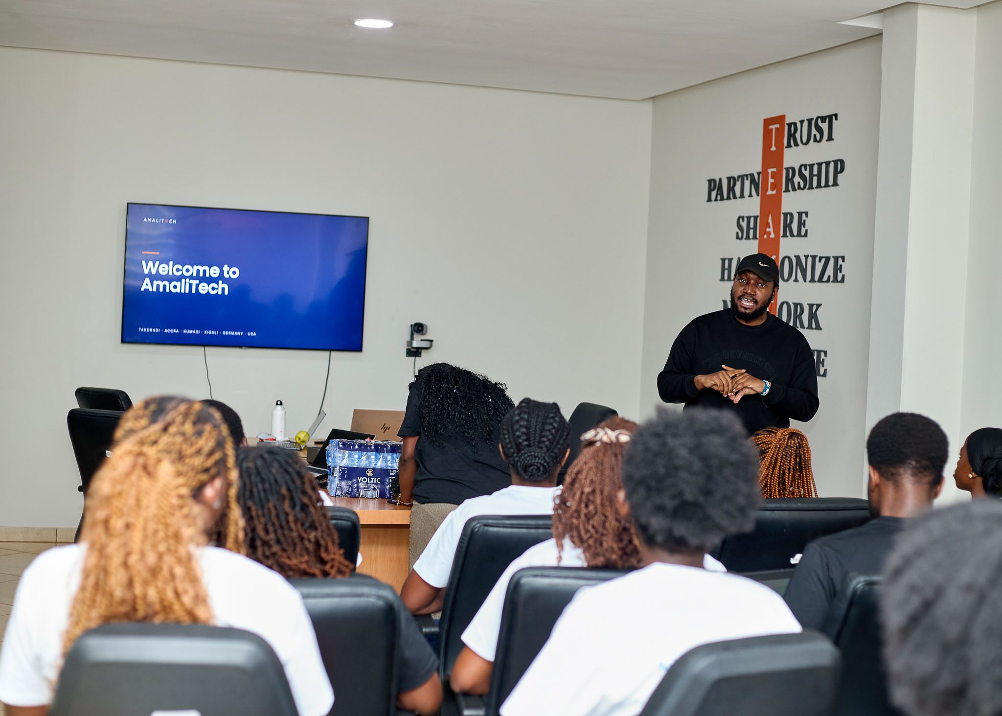 	Students seated in the AmaliTech Kumasi meeting room during the "Welcome to AmaliTech" session, beside the wall displaying the company's TEAM values.