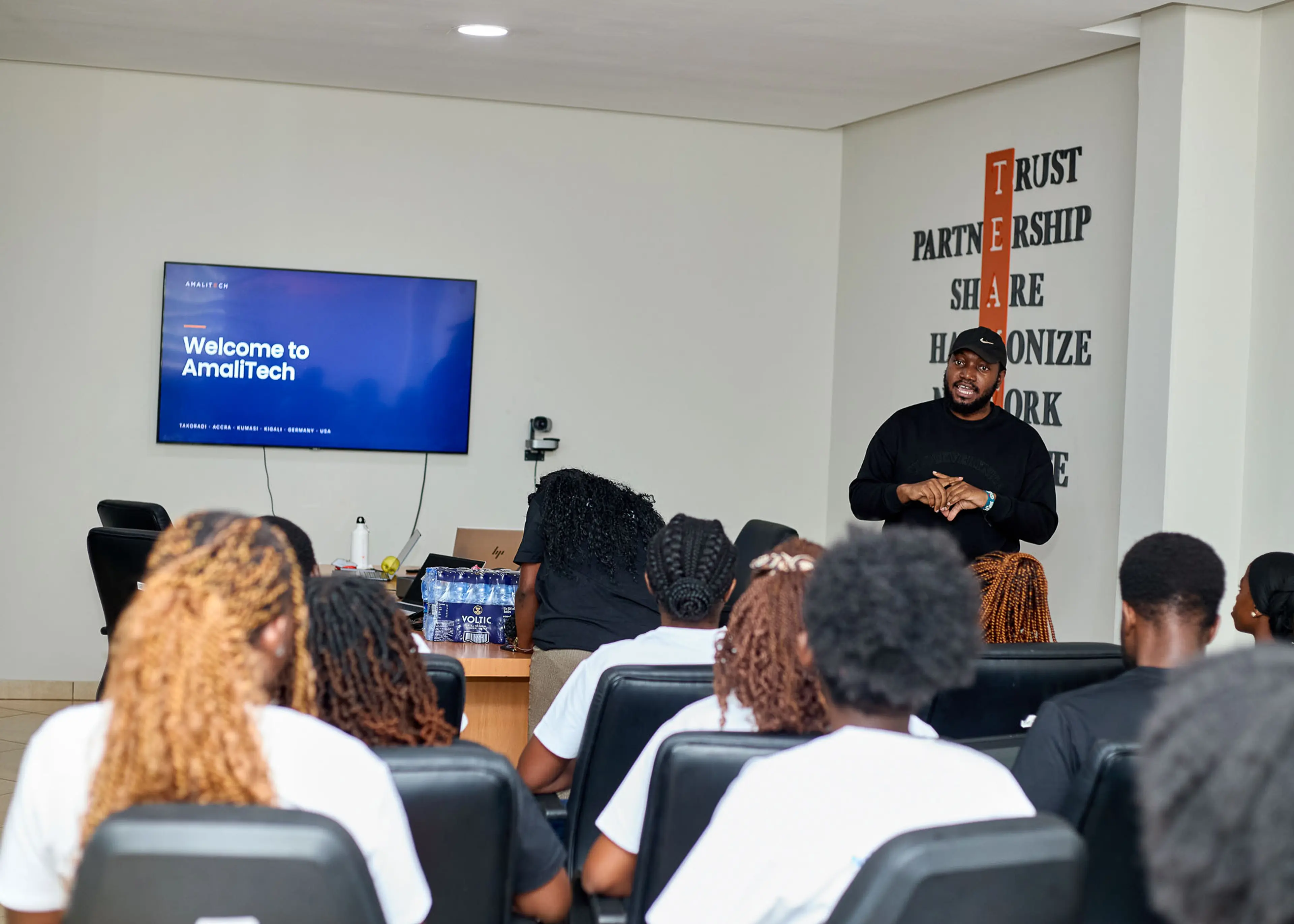 Students seated in the AmaliTech Kumasi meeting room during the "Welcome to AmaliTech" session, beside the wall displaying the company's TEAM values.