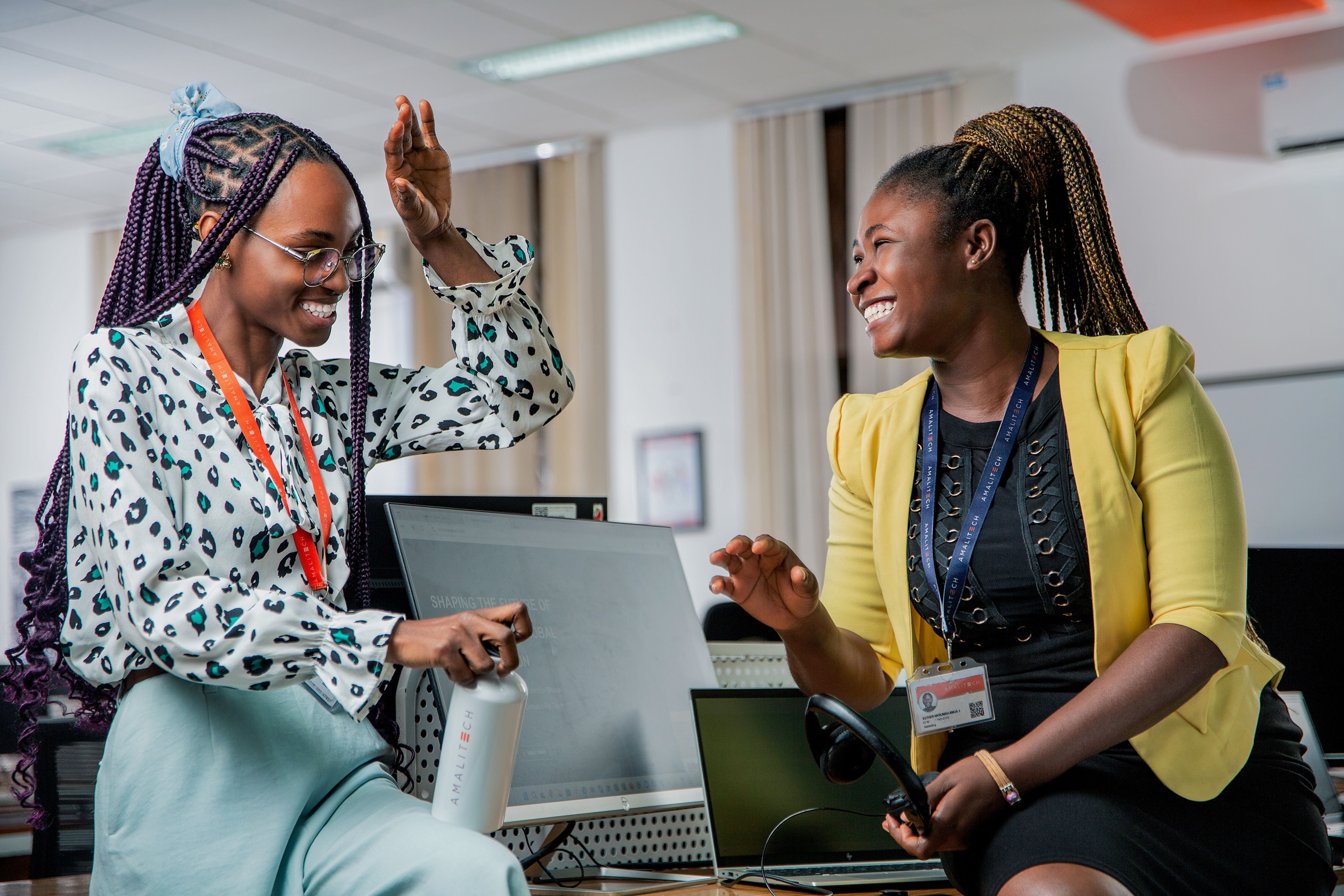 Two women sitting on a desk, laughing