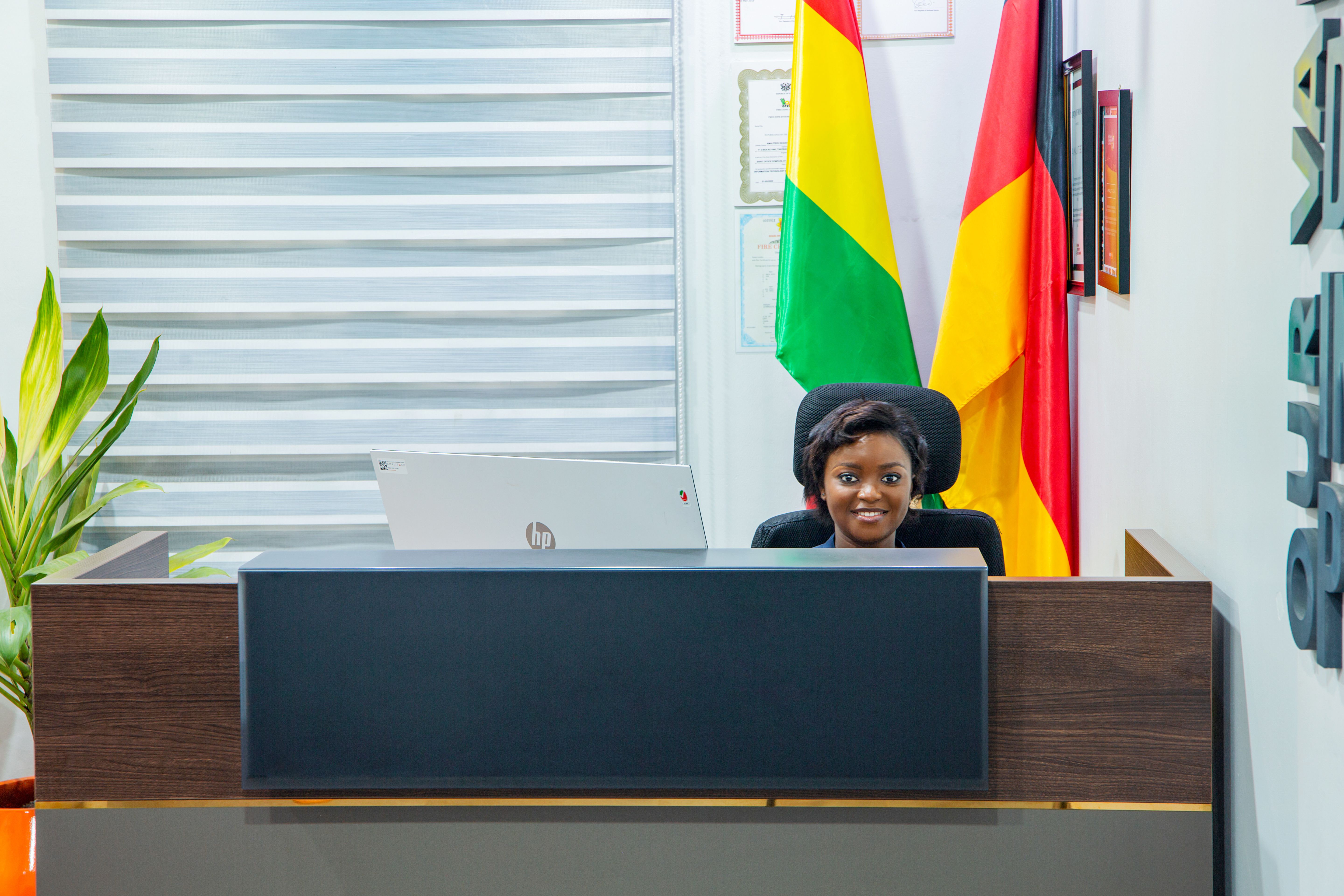 a picture of a lady seated at our Accra reception smiling, with AmaliTech inscribed on the wall, and Ghana and Germany flag