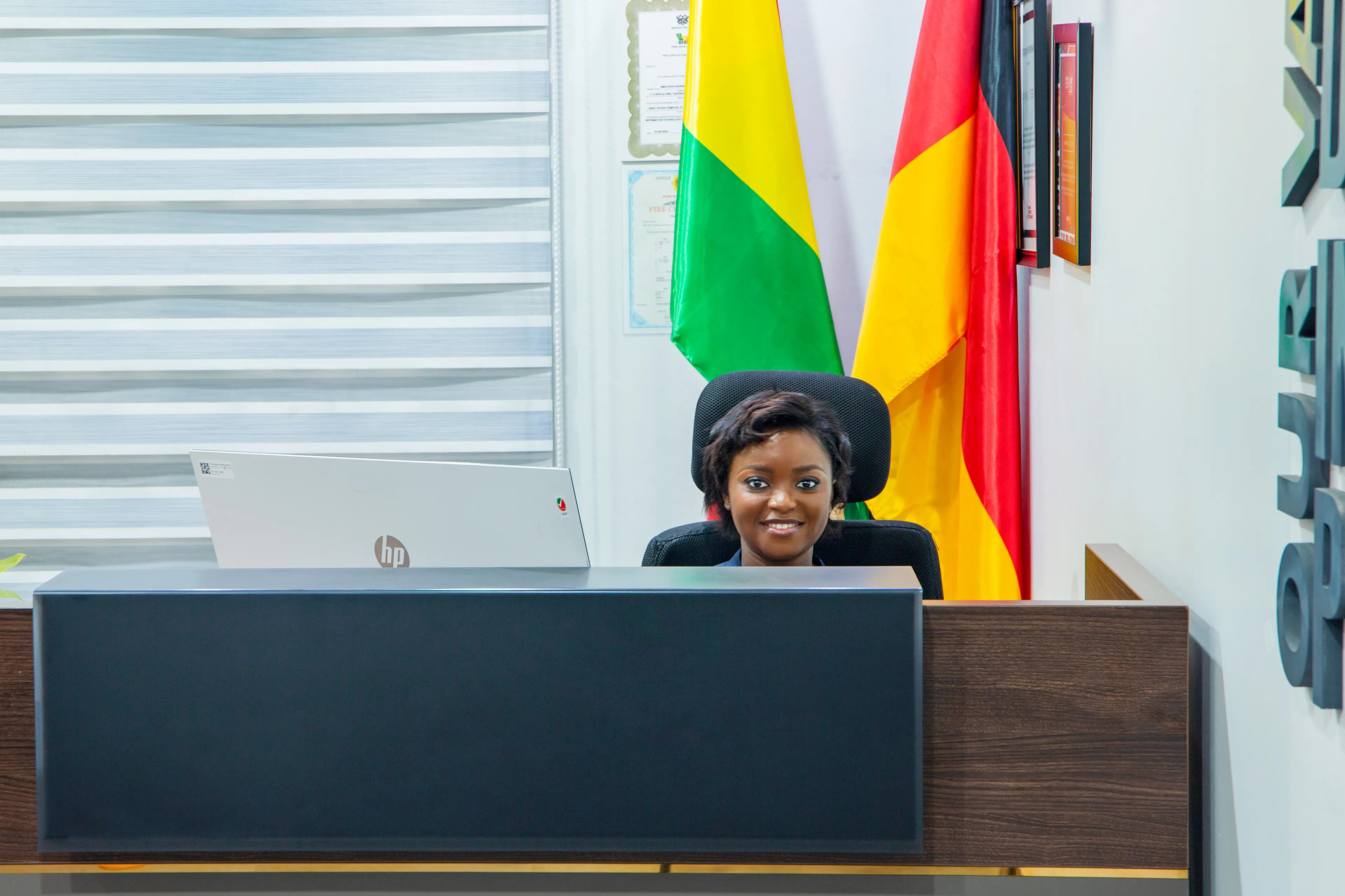 a picture of a lady seated at our Accra reception smiling, with AmaliTech inscribed on the wall, and Ghana and Germany flag
