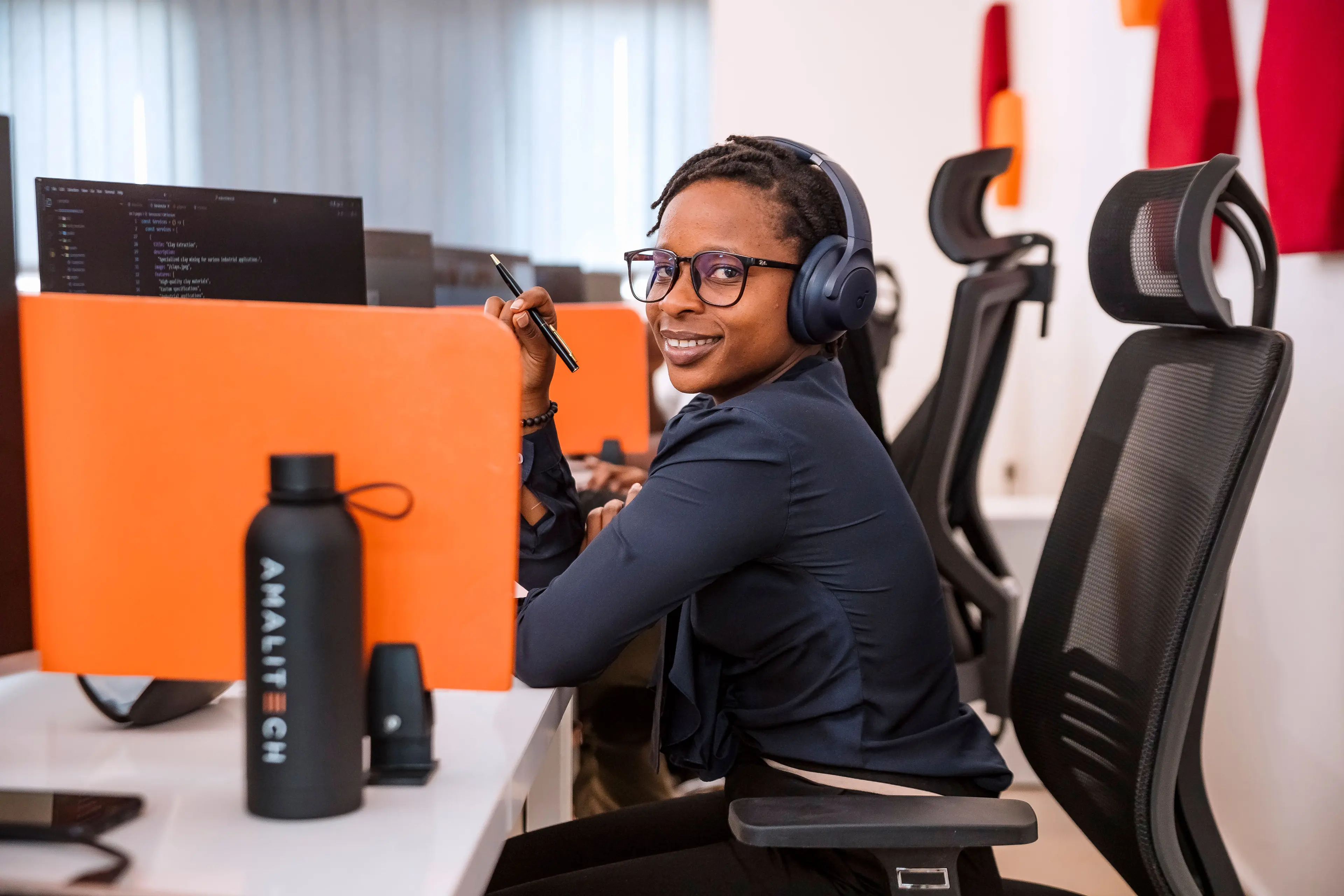 A women sitting at her desk, wearing headphones and smiling at the camera
