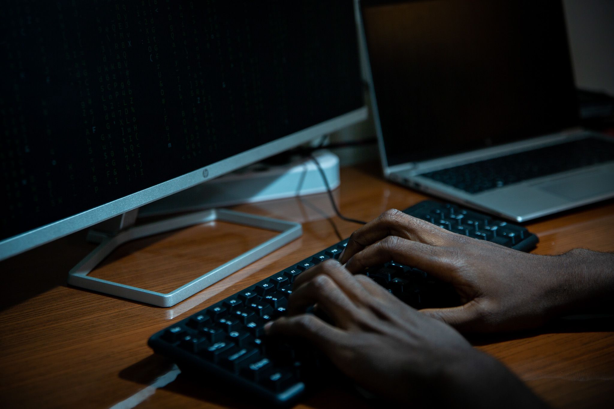 Close-up of a person typing on a keyboard in front of multiple computer screens