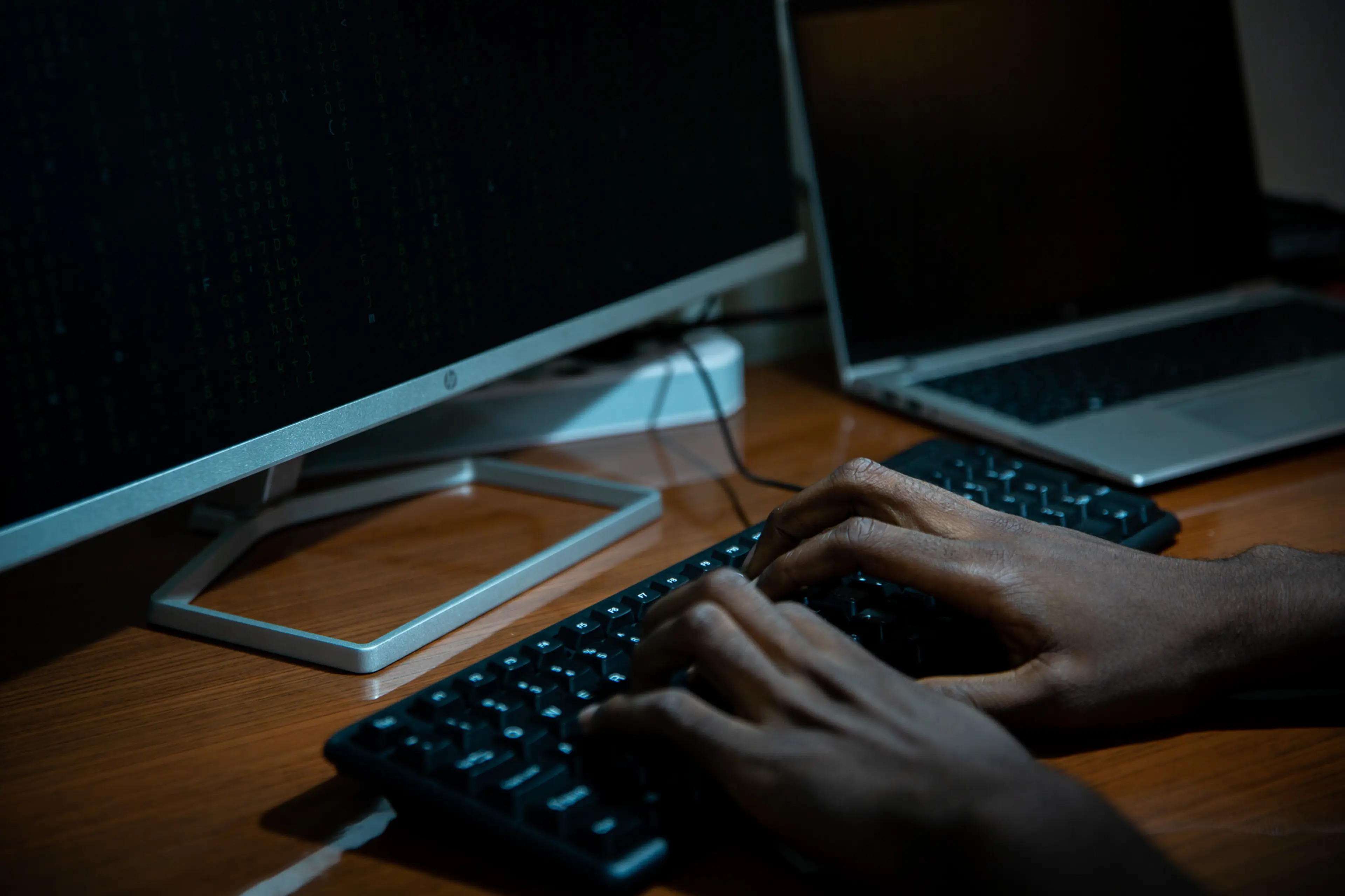 Close-up of a person typing on a keyboard in front of multiple computer screens