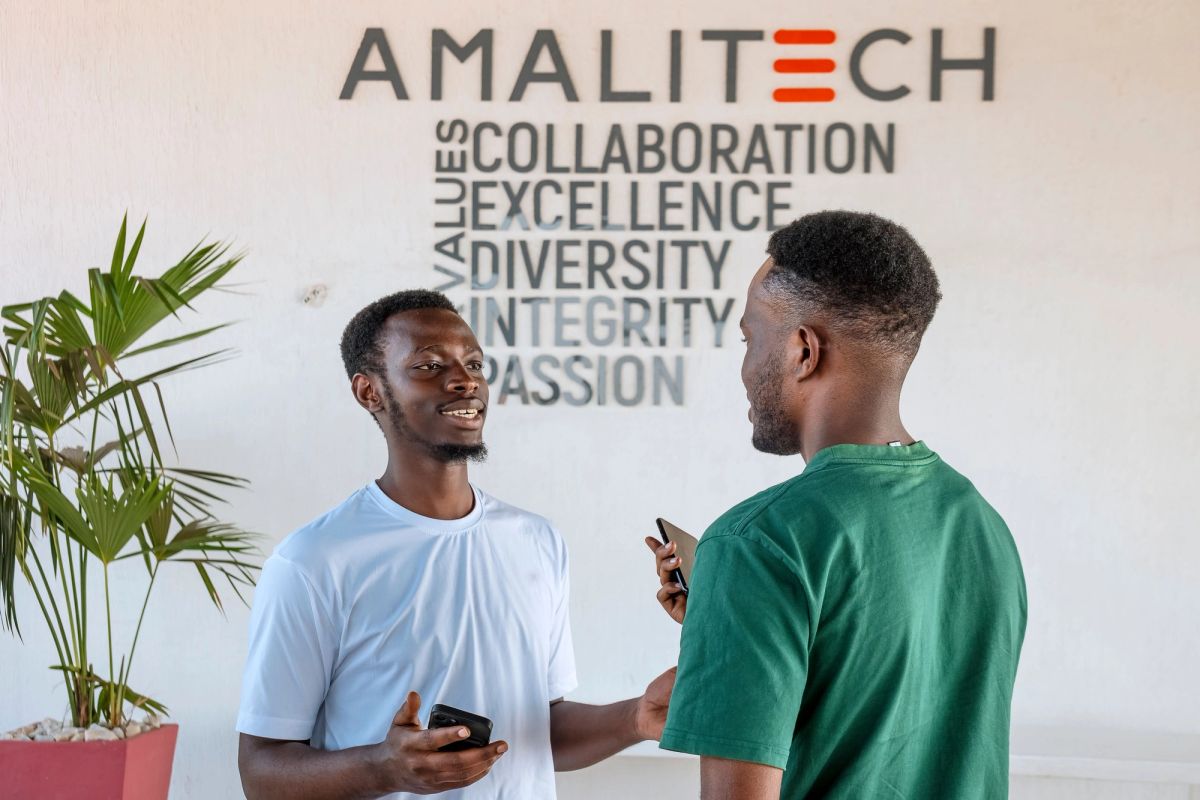 Two men talking in front of an AmaliTech sign that is showing our core values.