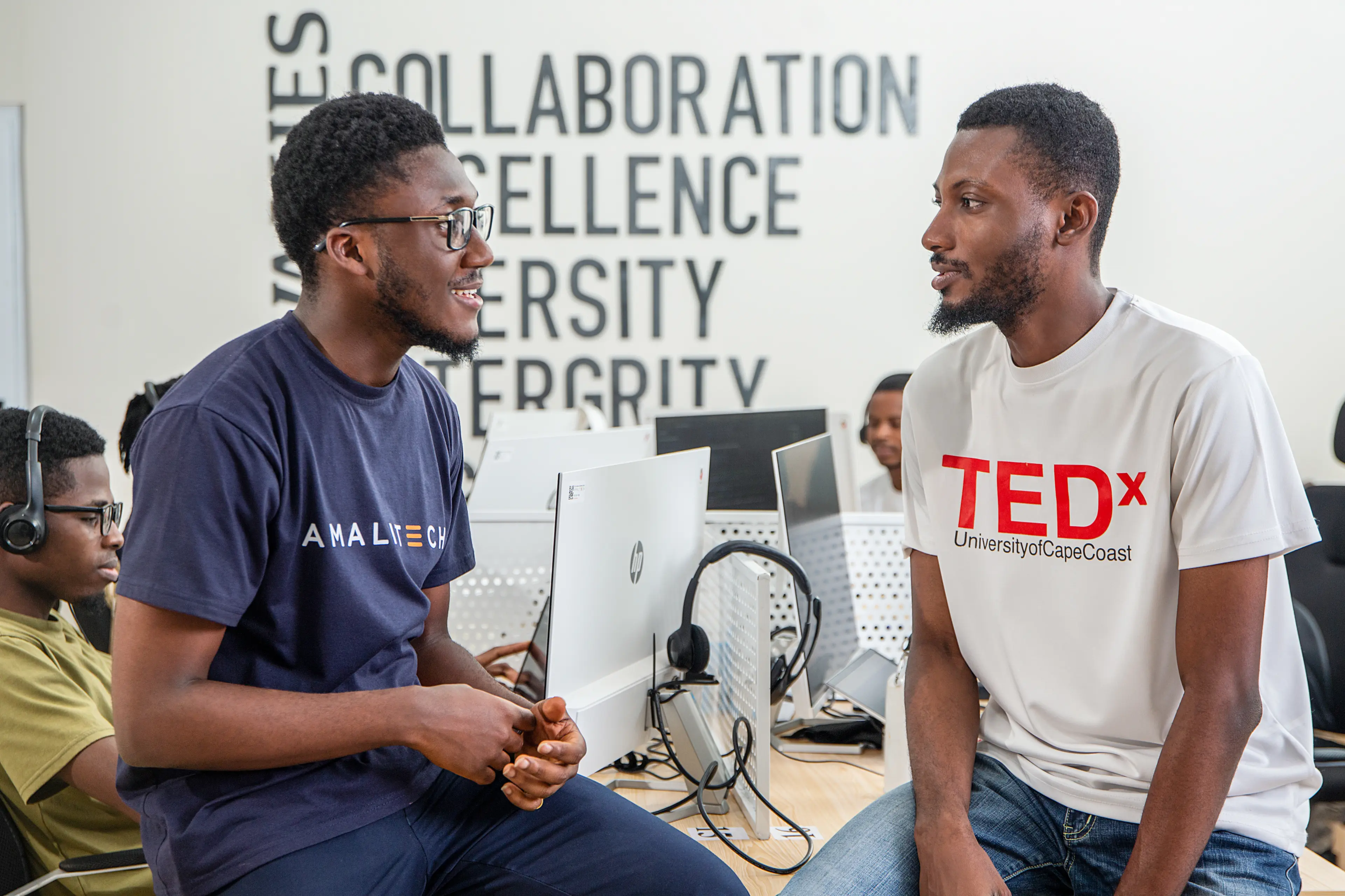 Two men sitting on a desk, in conversation