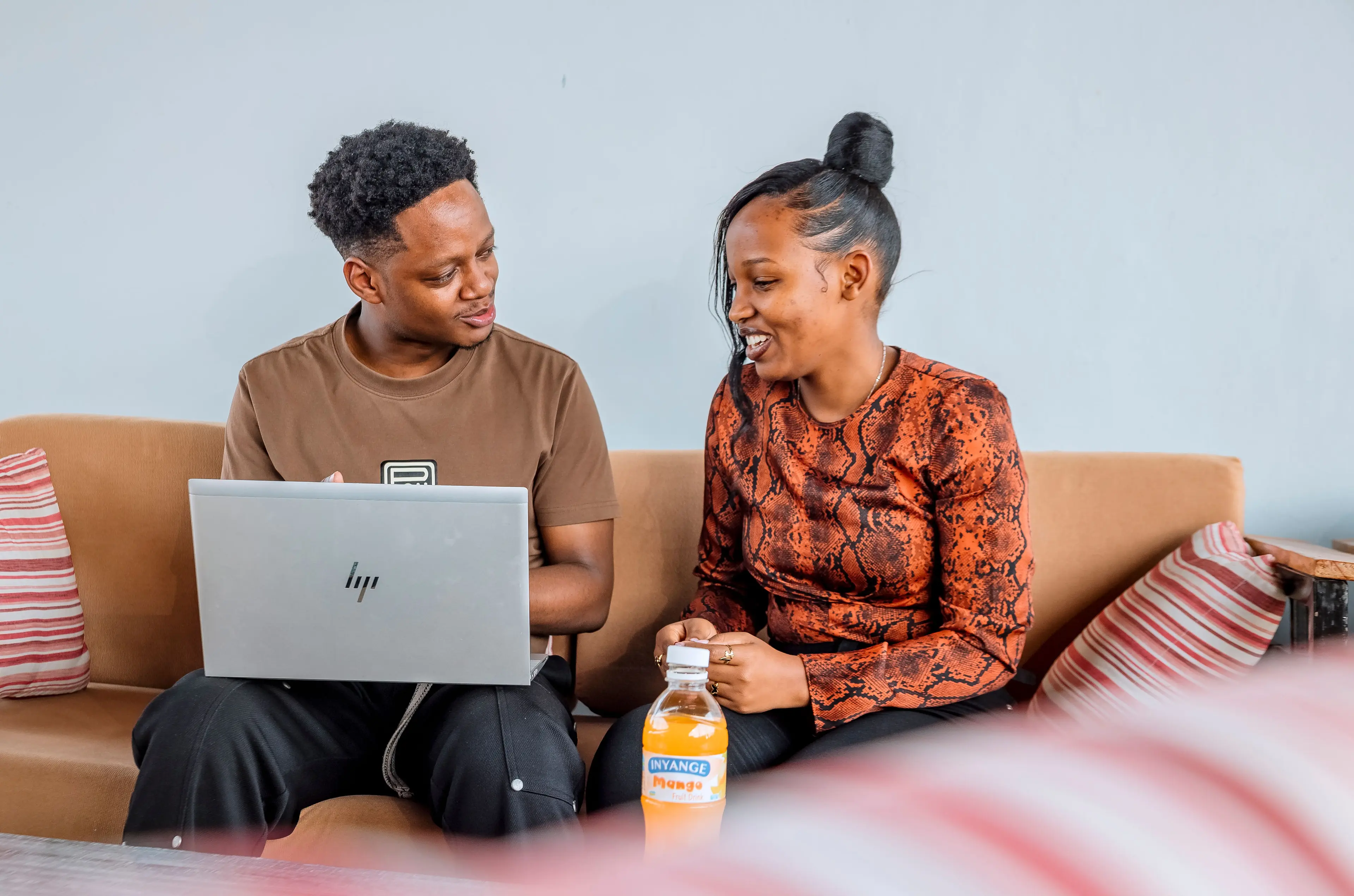 A man and a women sitting on the sofa, having a conversation while looking at a laptop