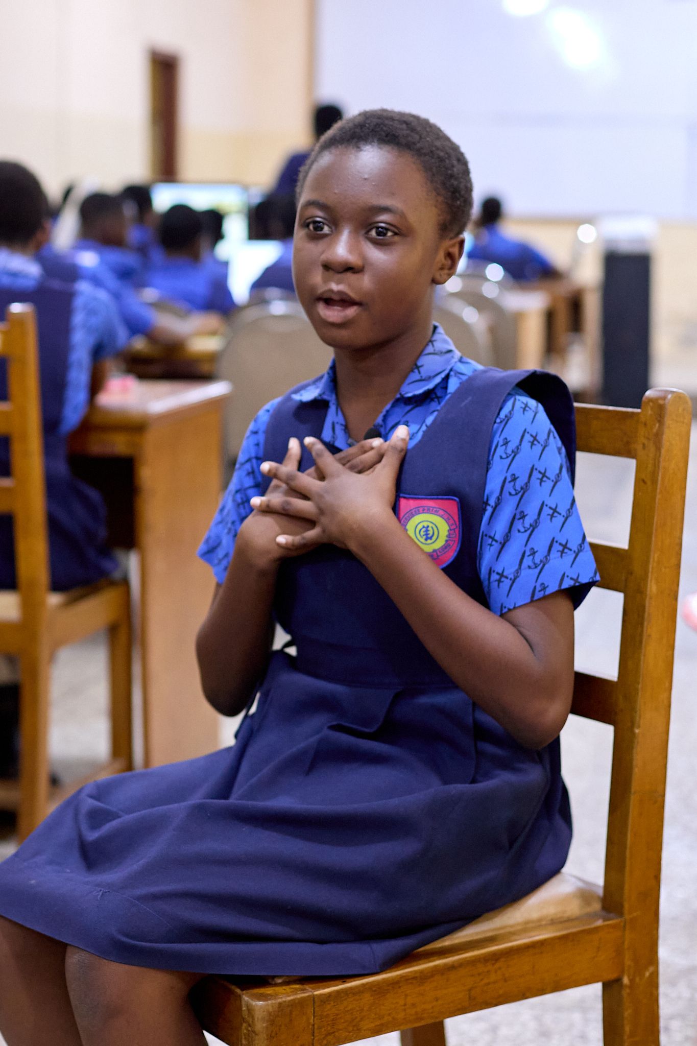 A girl sitting on a chair, wearing a blue uniform and talking