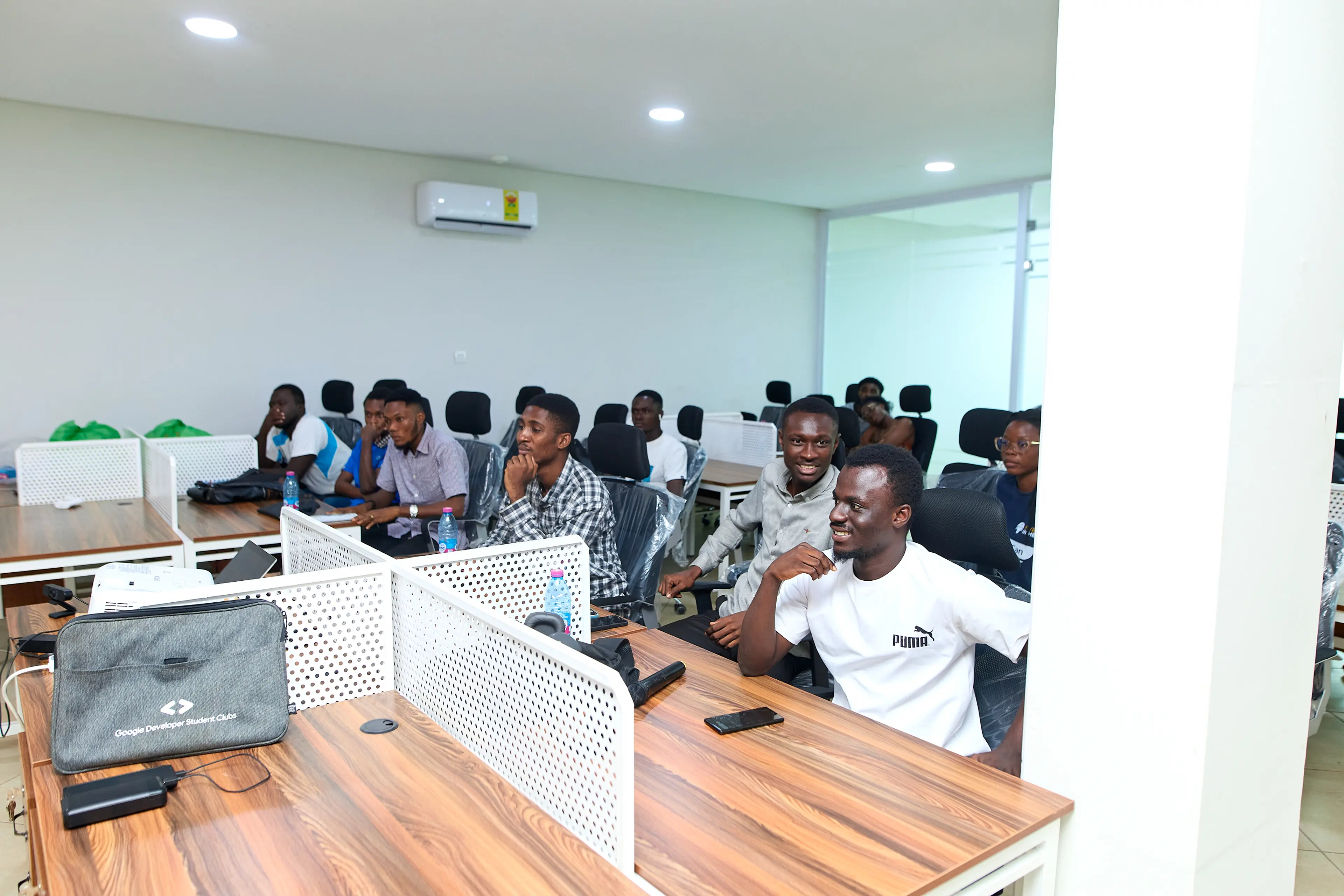 Young professionals seated at desks in a bright training room, listening attentively during a technology-focused learning session.