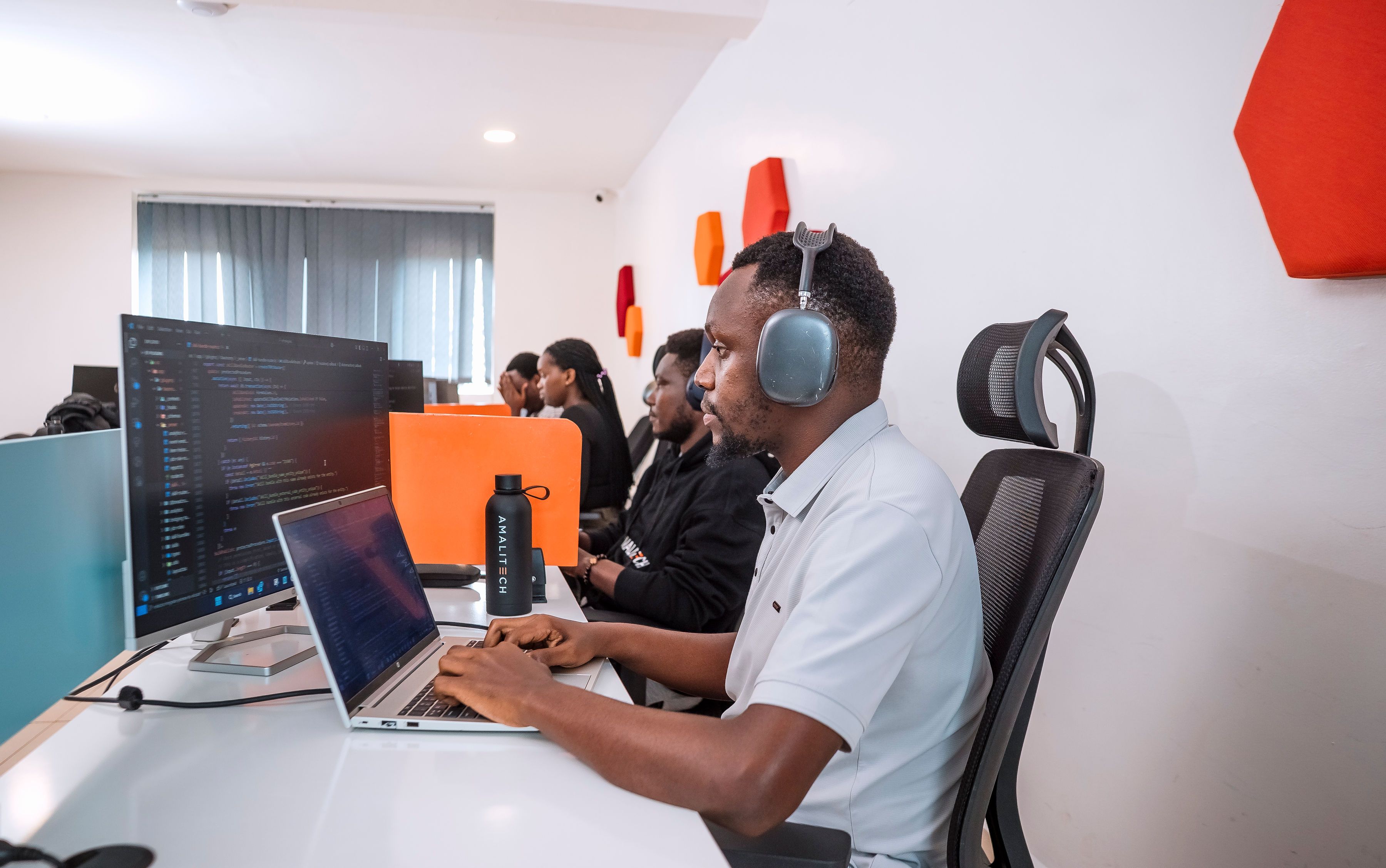 Four people sitting in a row at their desks, working on their computers