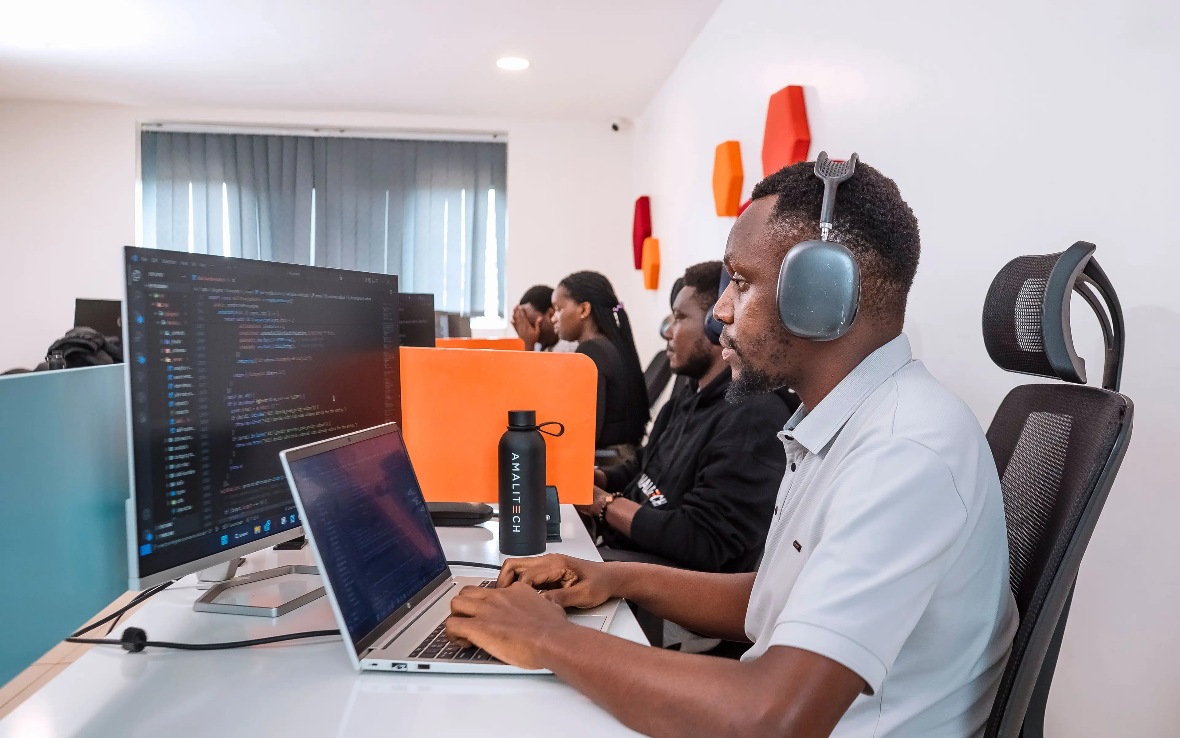 Four people sitting in a row at their desks, working on their computers