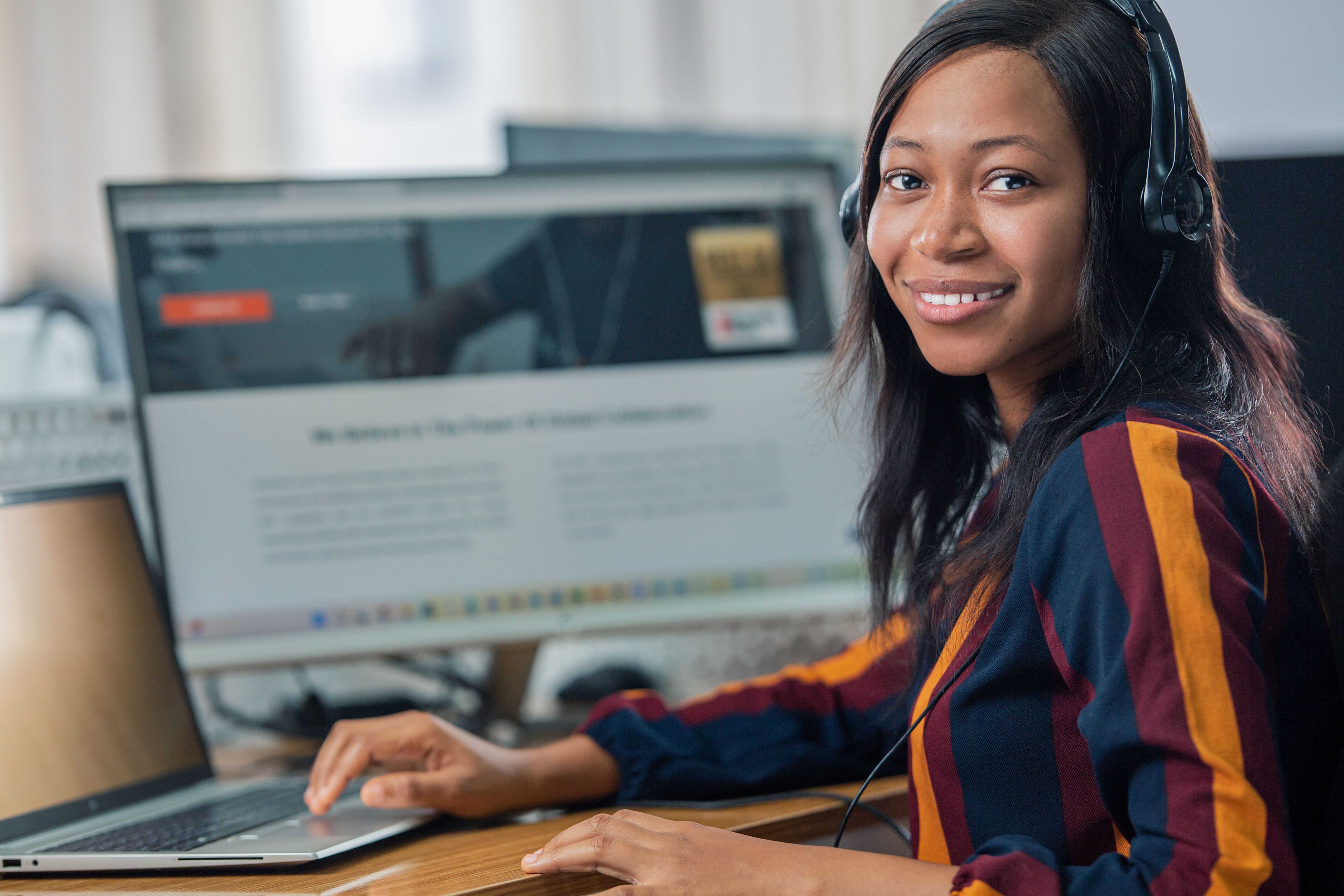 A women sitting at her desk, looking over her shoulder towards the camera and smiling