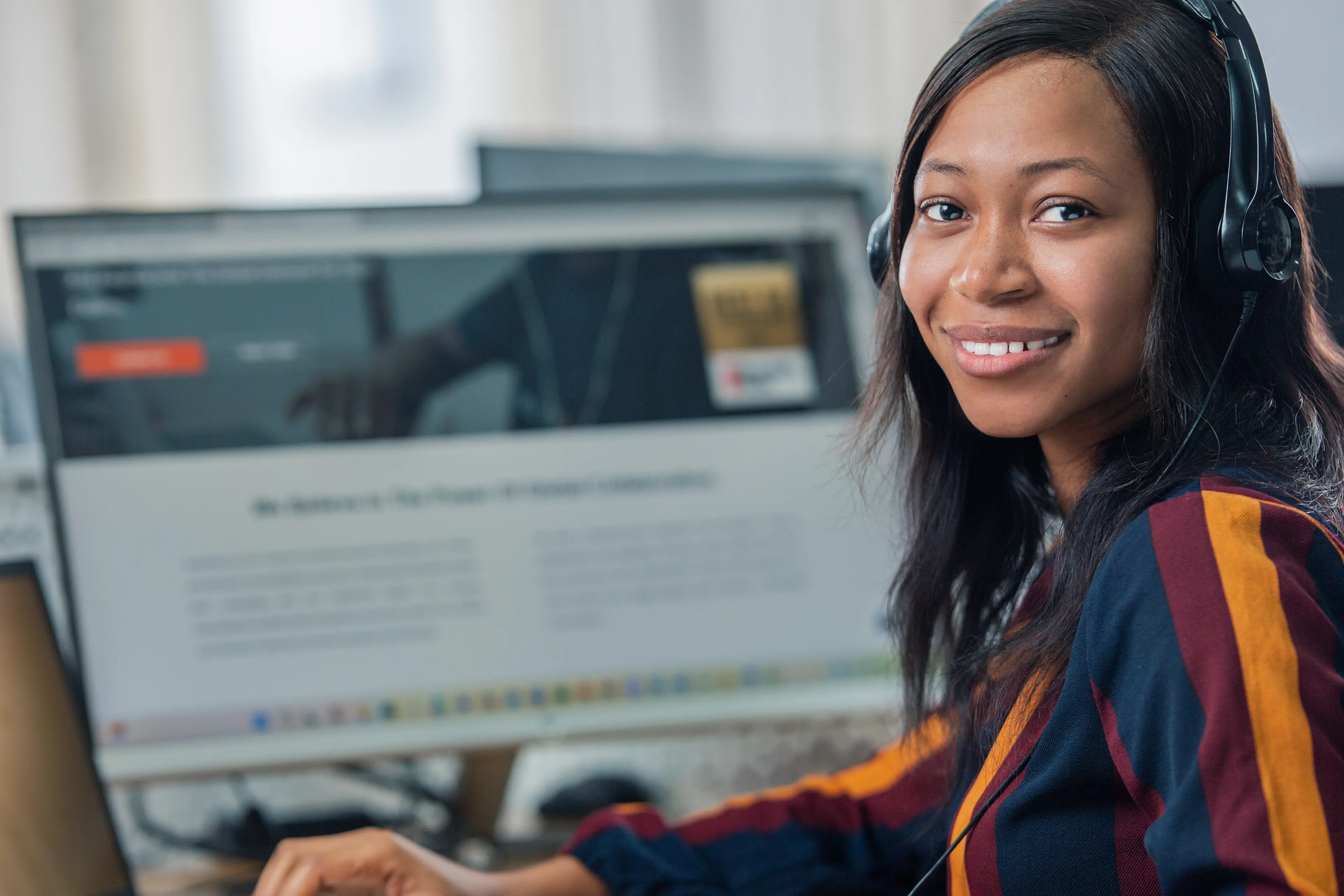 A women sitting at her desk, looking over her shoulder towards the camera and smiling