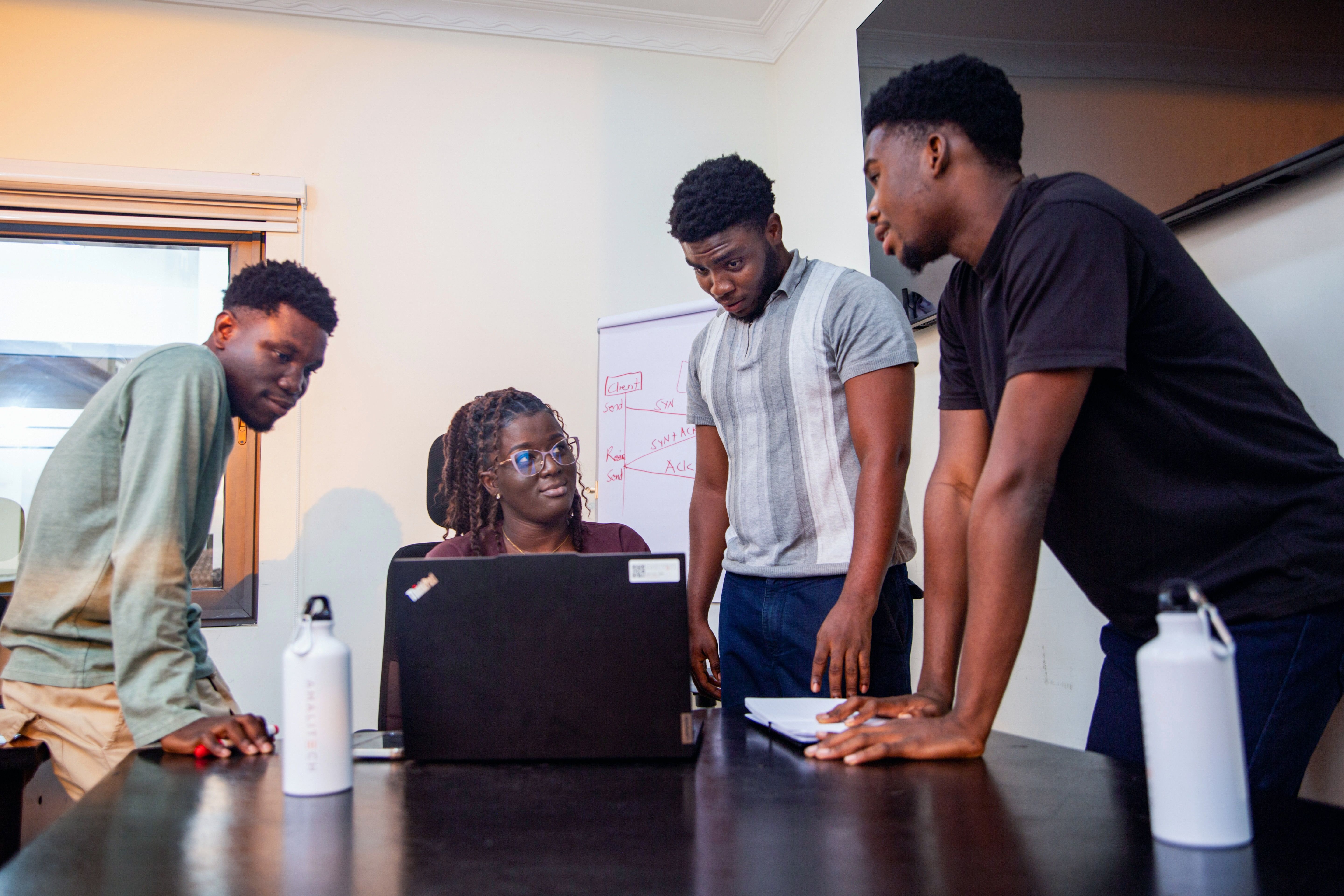 Four people sitting and standing near a desk, in discussion.
