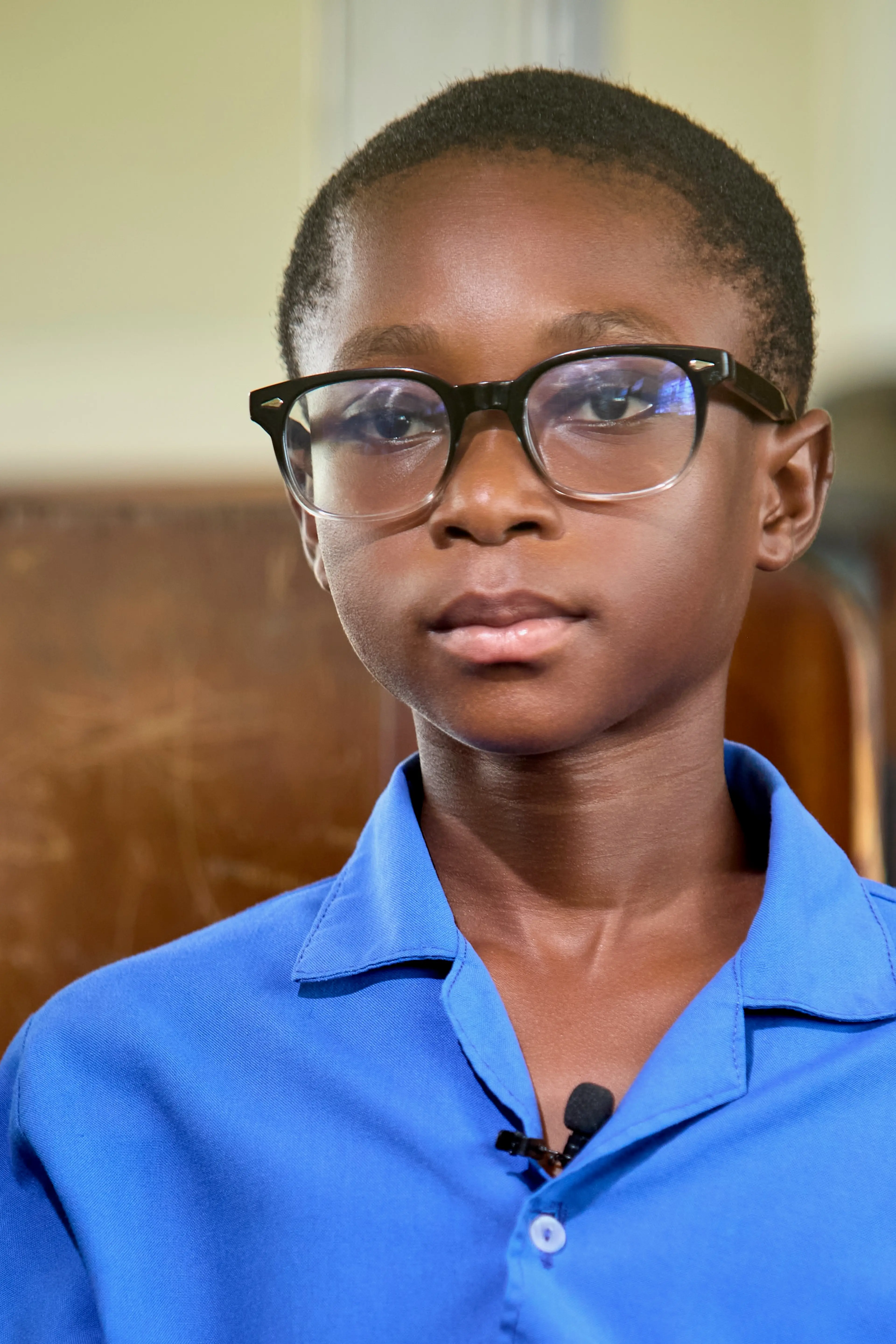 A child wearing glasses, sitting on a chair, and facing the camera