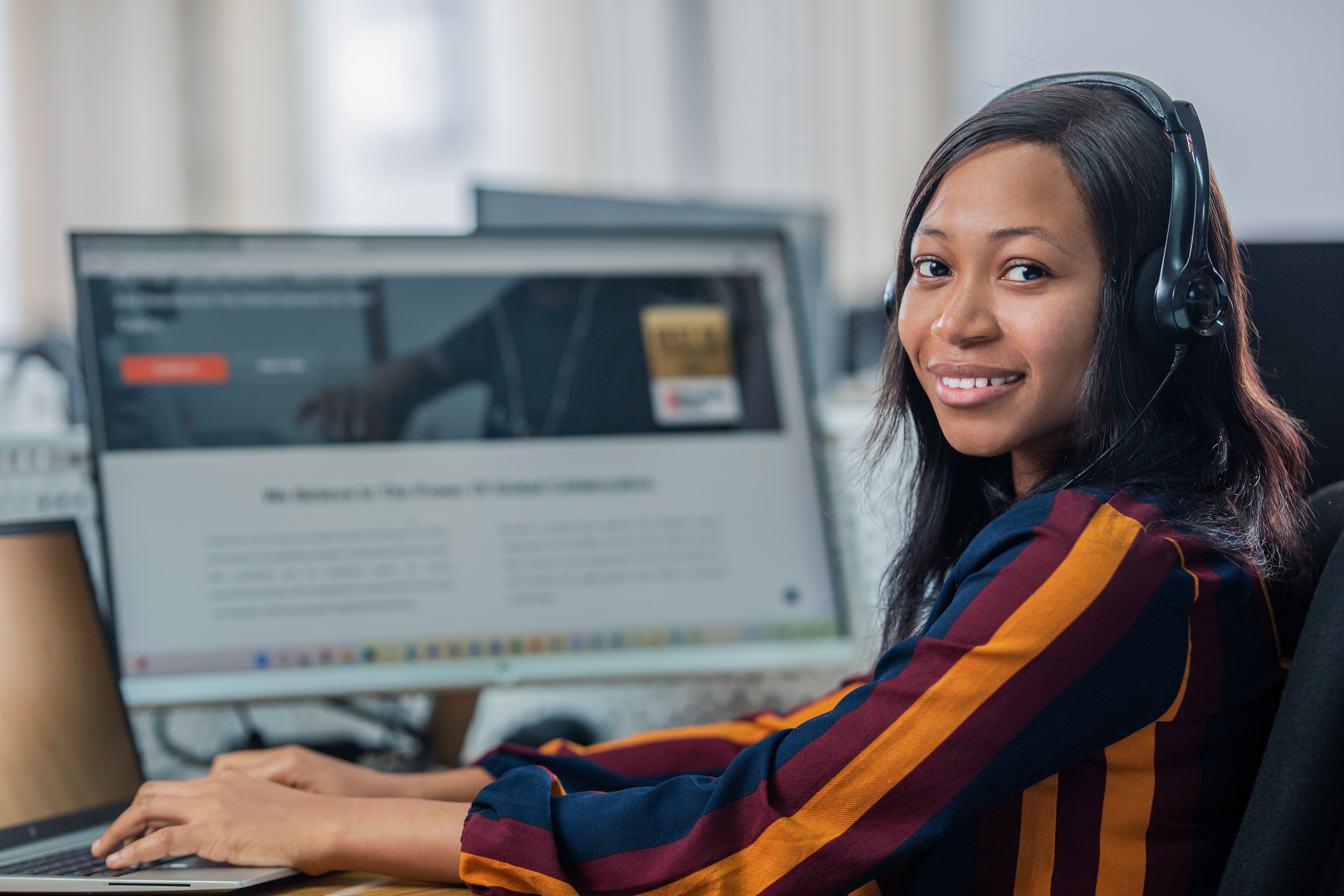 A women smiling at the camera, over her shoulder - wearing a headset