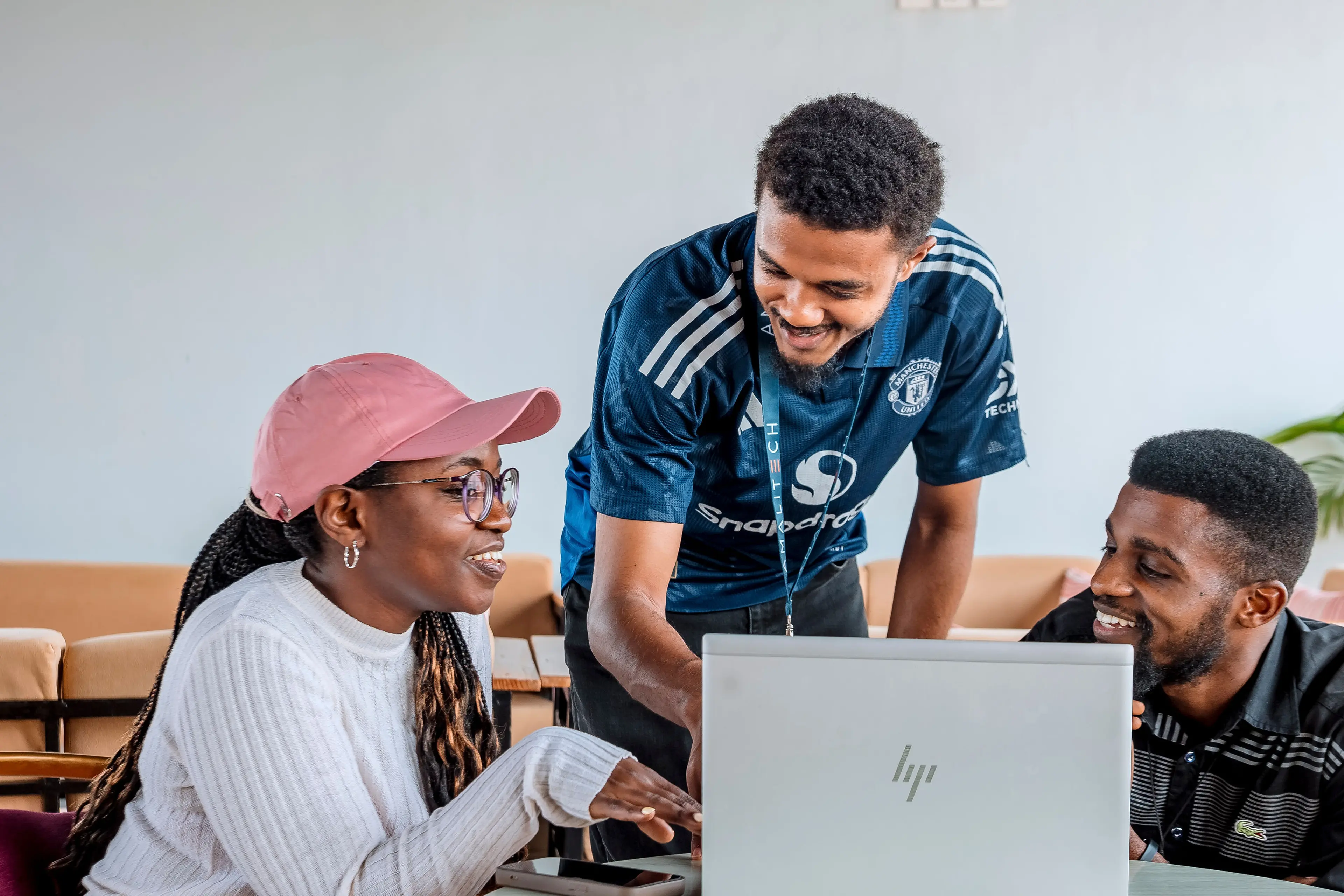 Three people sitting and standing infront of a computer, talking