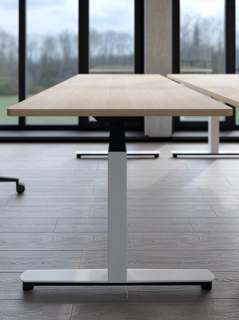 Seitenansicht des 25-table R von Klain mit elegant geformtem Tischbein, abgerundetem Fußausleger und höhenverstellbarem Gestell in einem modernen Büro.