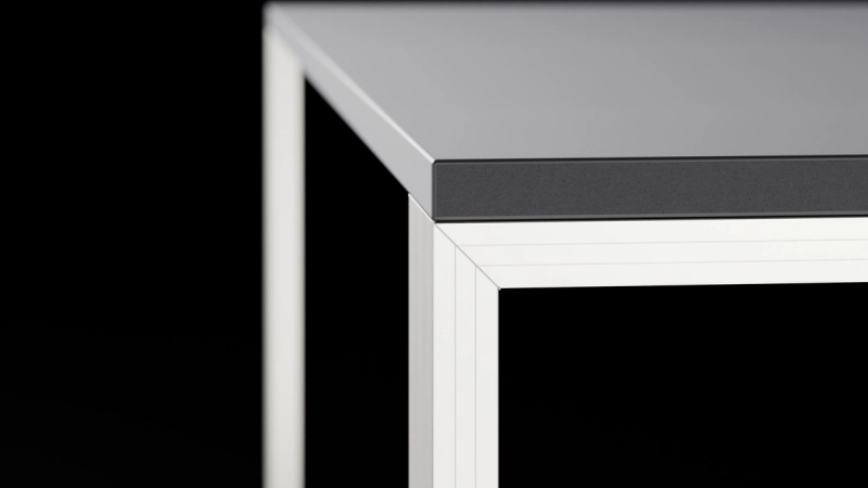 Detailaufnahme der Tischecke mit anthrazitfarbener Platte und hellem Aluminiumrahmen vor dunklem Hintergrund.