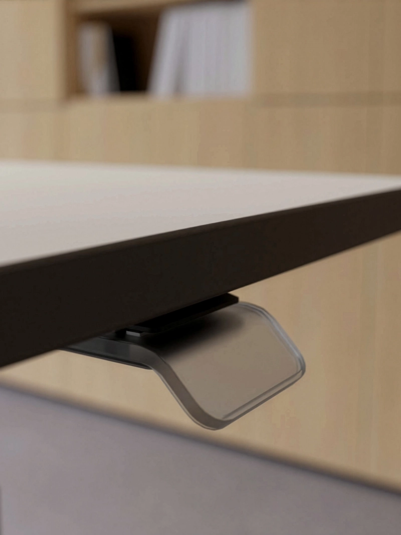 Detailaufnahme des Bedientasters des höhenverstellbaren 25-table Q von Klain. Die Nahansicht zeigt den nahezu transparenten Kunststoffhebel zur komfortablen Steuerung der elektrischen Höhenverstellung und unterstreicht die hochwertige Verarbeitung des Schreibtisches.