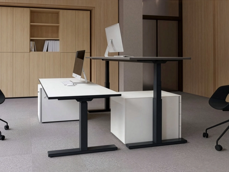 Ambienteaufnahme mit zwei höhenverstellbaren 25-table Q Schreibtischen von Klain in einem modernen Büro. Die unterschiedlichen Arbeitshöhen zeigen die ergonomische Flexibilität, das funktionale Design und die vielseitigen Einsatzmöglichkeiten des Schreibtisches.  SEO-optimierter A