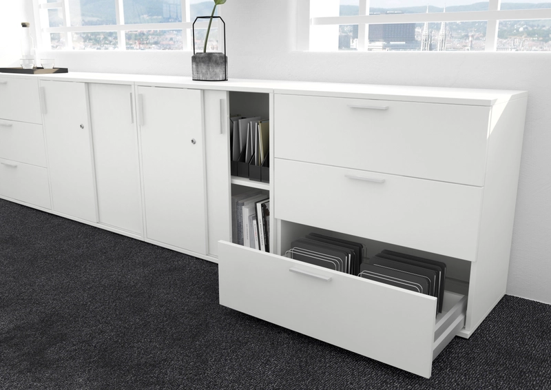 Weißes Simplus-Sideboard aus Schiebetürenschränken, offenem Regalfach und einem Schubladenschrank mit ausgezogener Schublade voller Hängemappen.