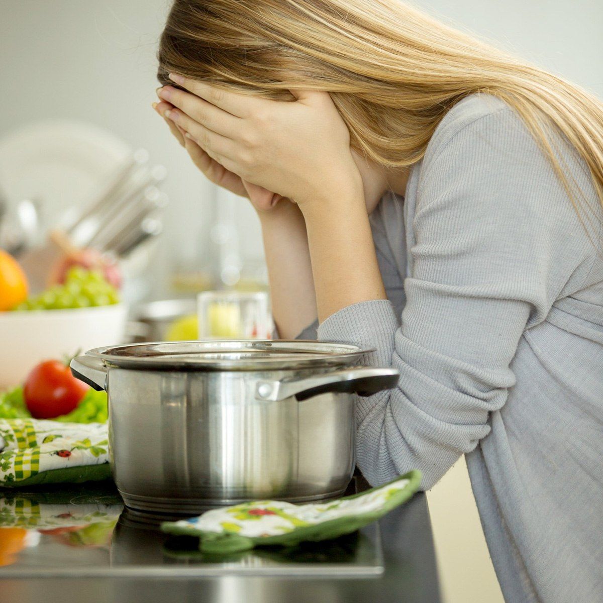 Mujer con el rostro entre las manos junto a una olla en la cocina.