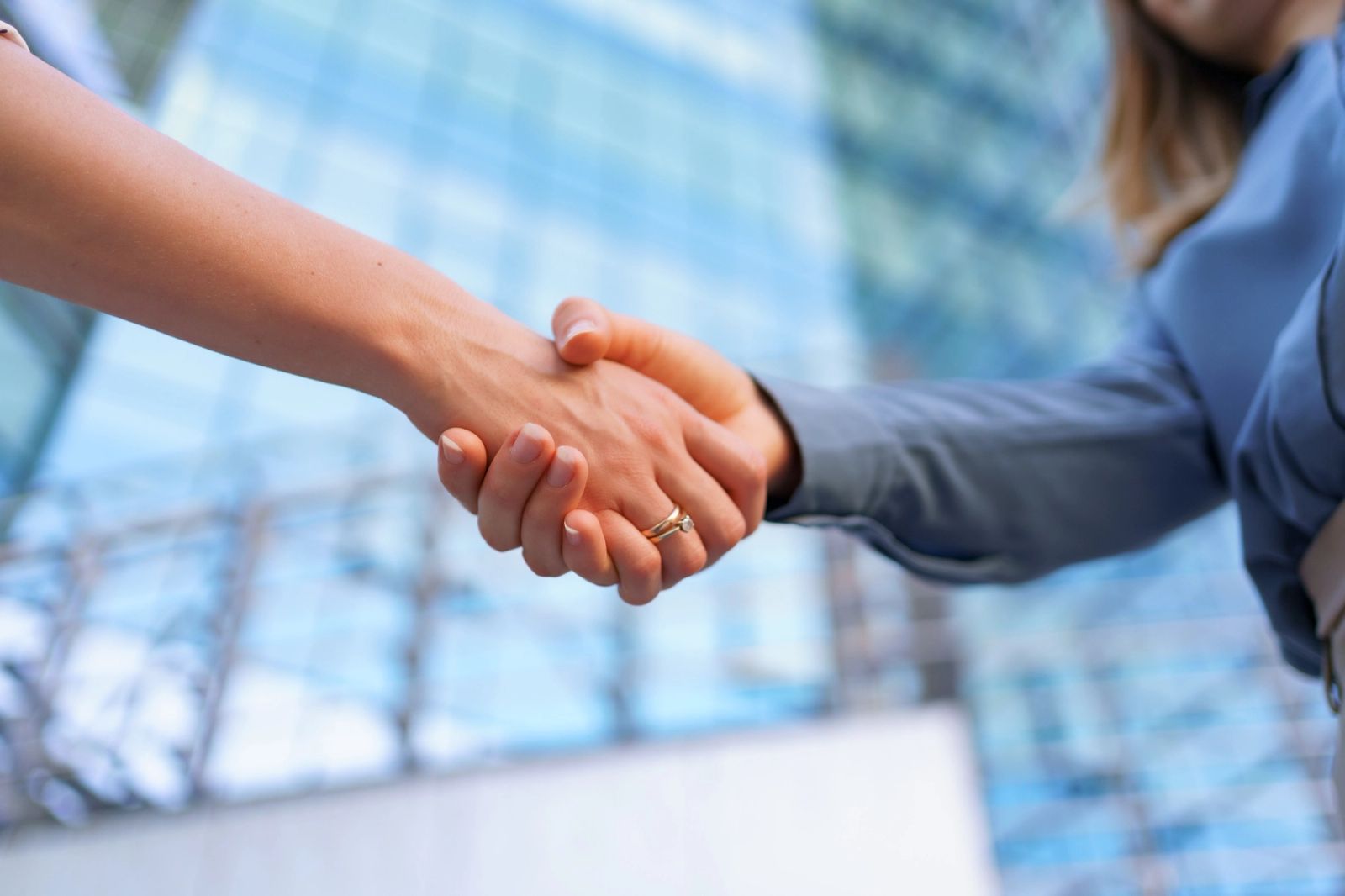 Two businesswomen shaking hands in front of a modern glass office building