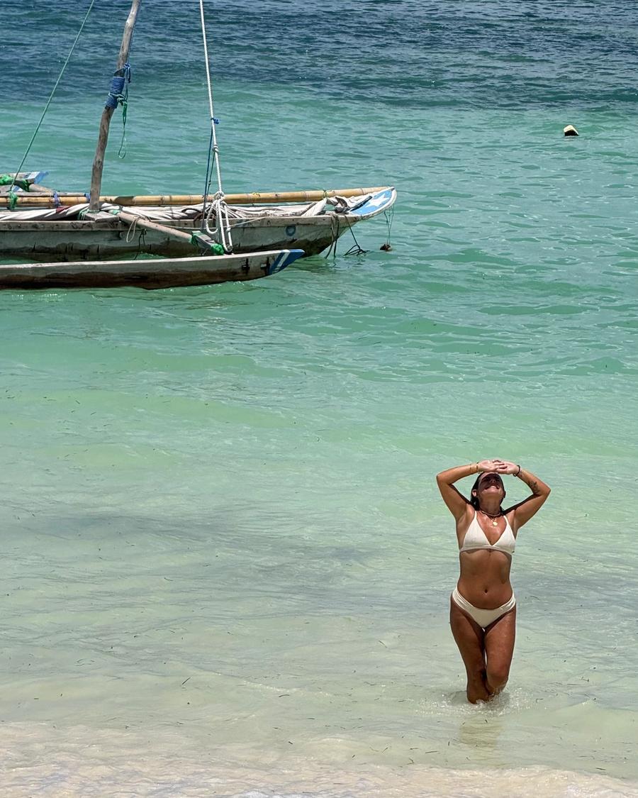 Mulher em água pela canela em Jambiani, com um dhow atrás.