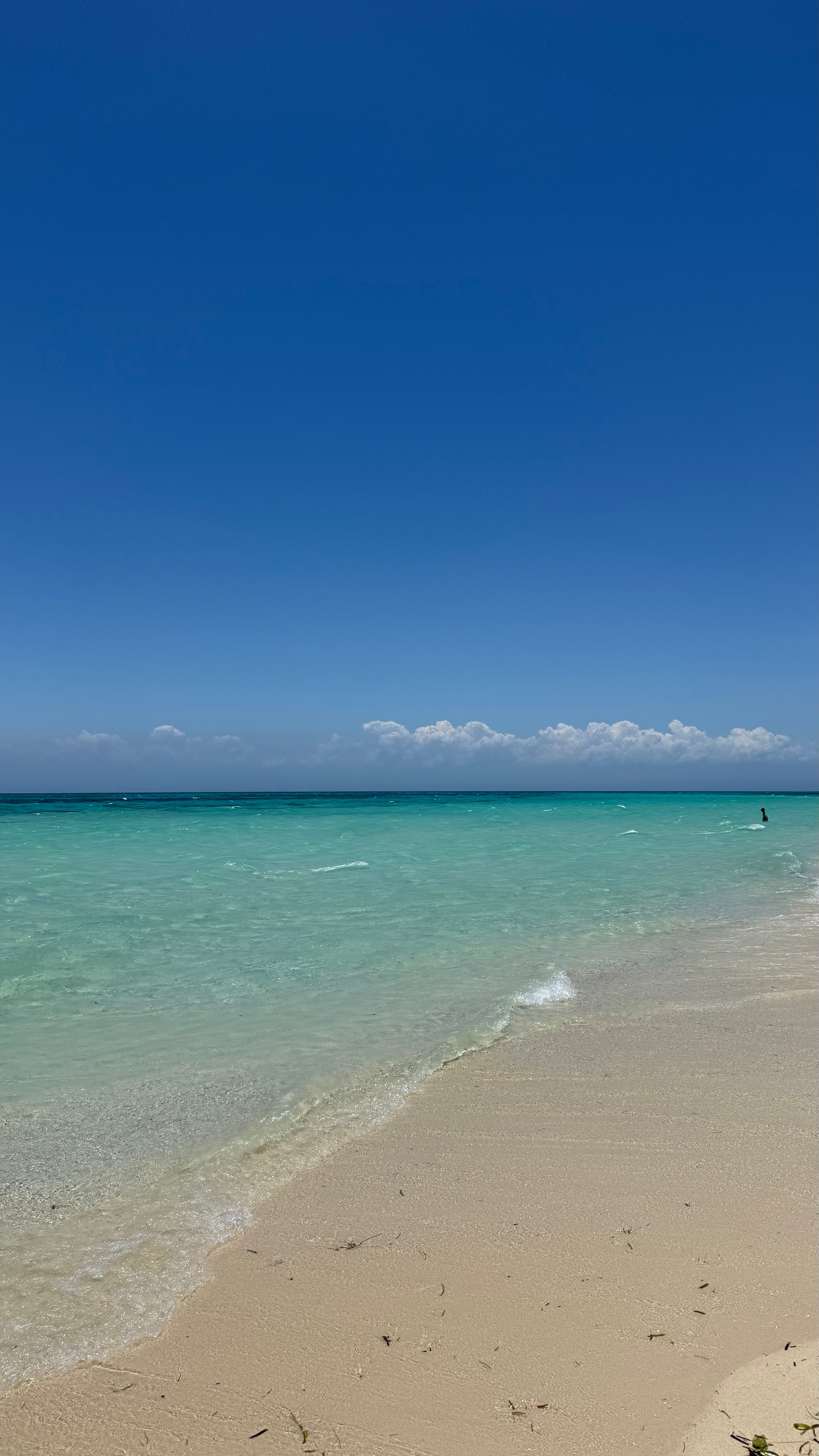 Praia quase vazia, areia branca e mar em tons de azul.