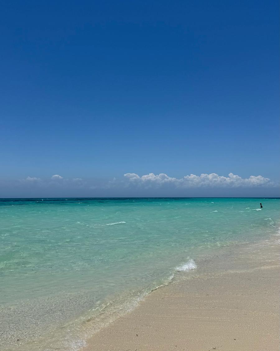 Praia quase vazia, areia branca e mar em tons de azul.
