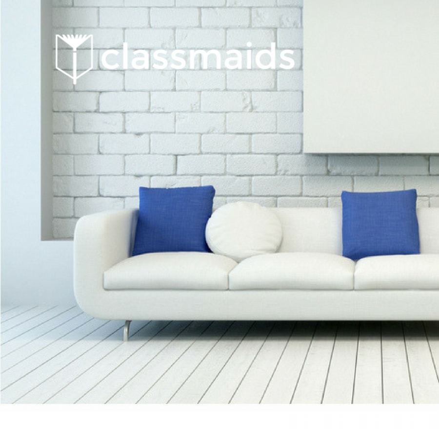 White sofa with blue cushions against a white brick wall and pale wood floor