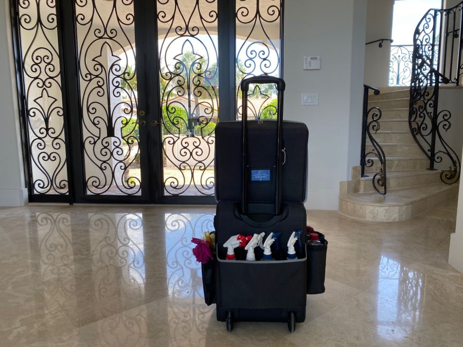 A cleaning caddy of supplies on a marble floor in a home entrance with wrought-iron doors