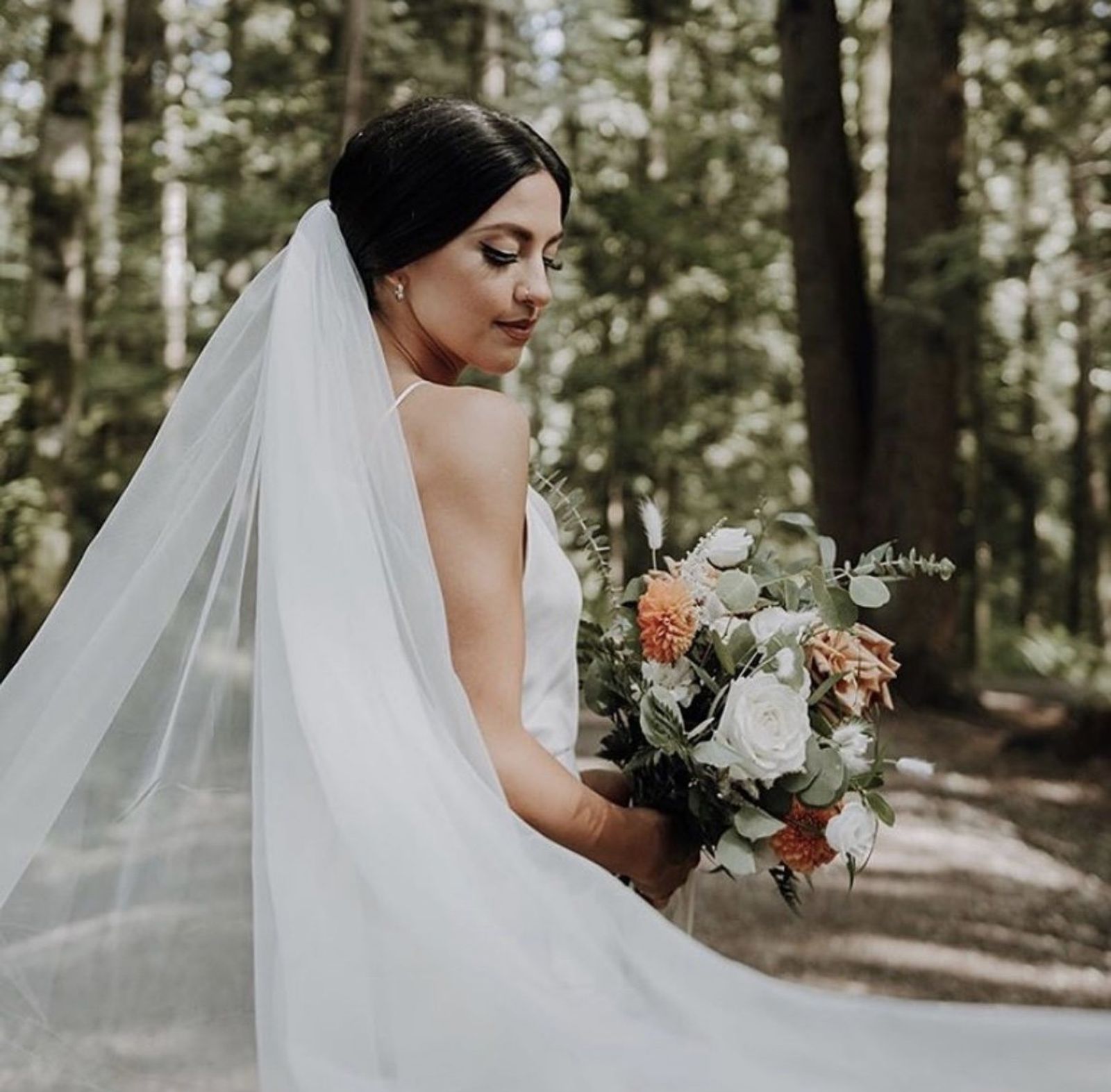 A bride in a forest with her veil and bouquet