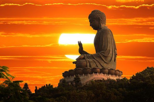 A large seated Buddha statue against an orange sunset.