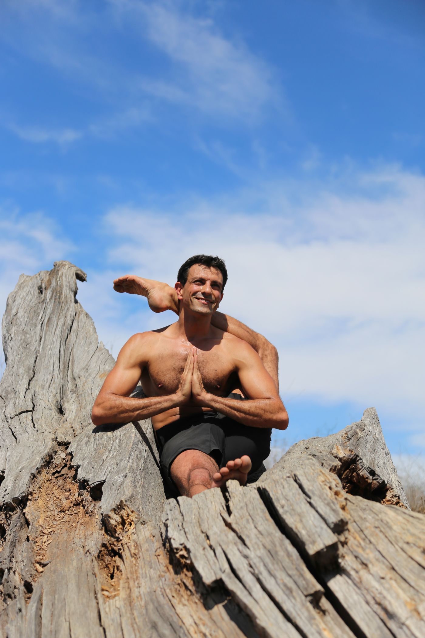 Doron seated on a tree stump, hands together, a foot held behind his head.