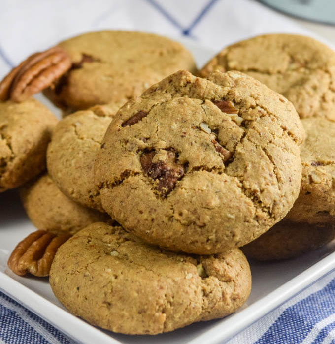 Pecan cookies on a white plate, with pecan halves beside them.