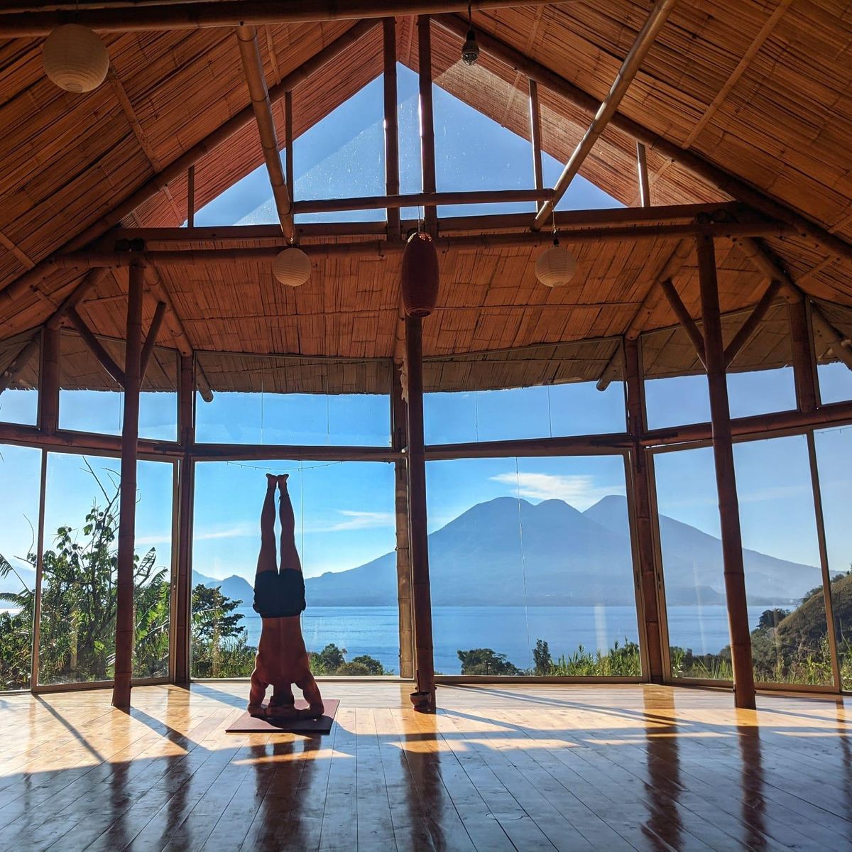 A headstand in a wooden shala with the lake behind.