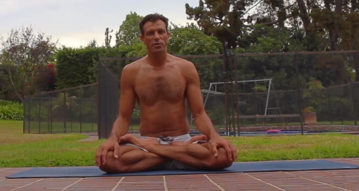 Doron seated in lotus on a mat outdoors.