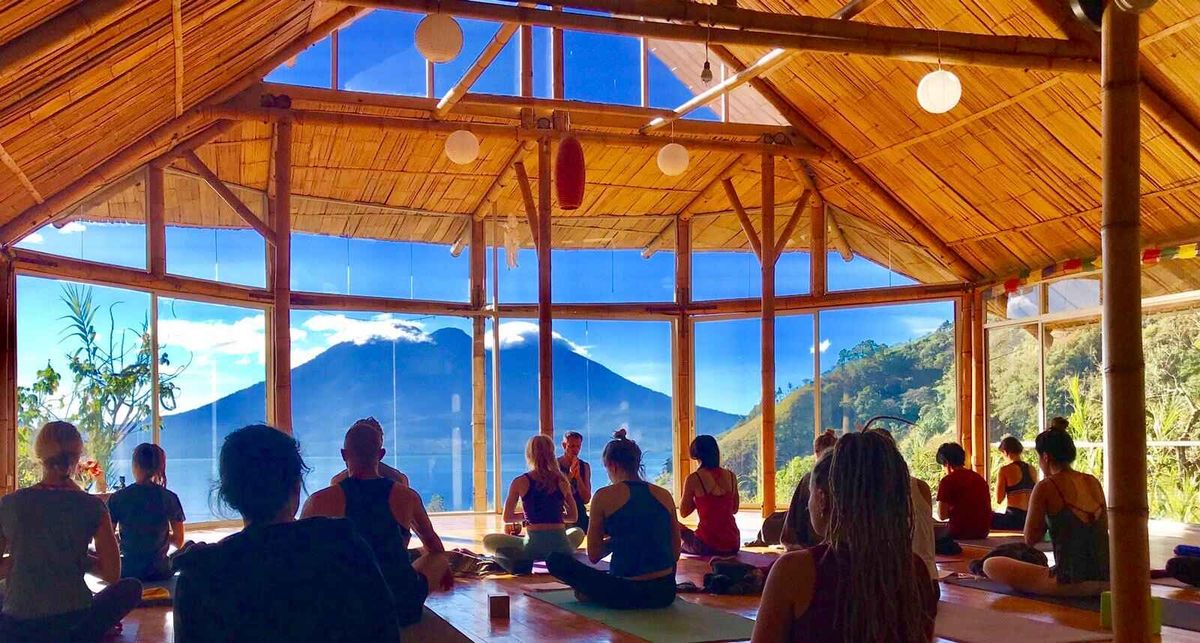 A class seated together on the floor of a wooden shala, facing the lake.