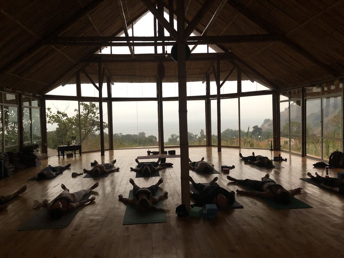A class resting in savasana in a wooden shala.