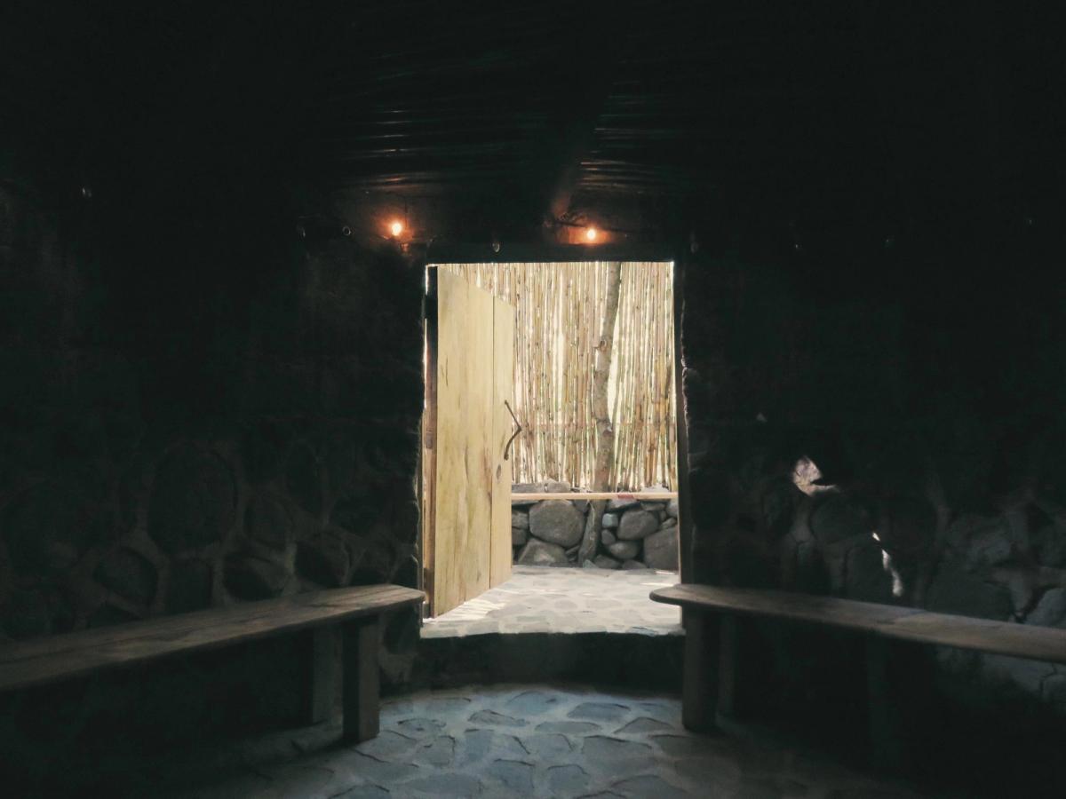 The dark interior of a temazcal, with a low door and a bench.