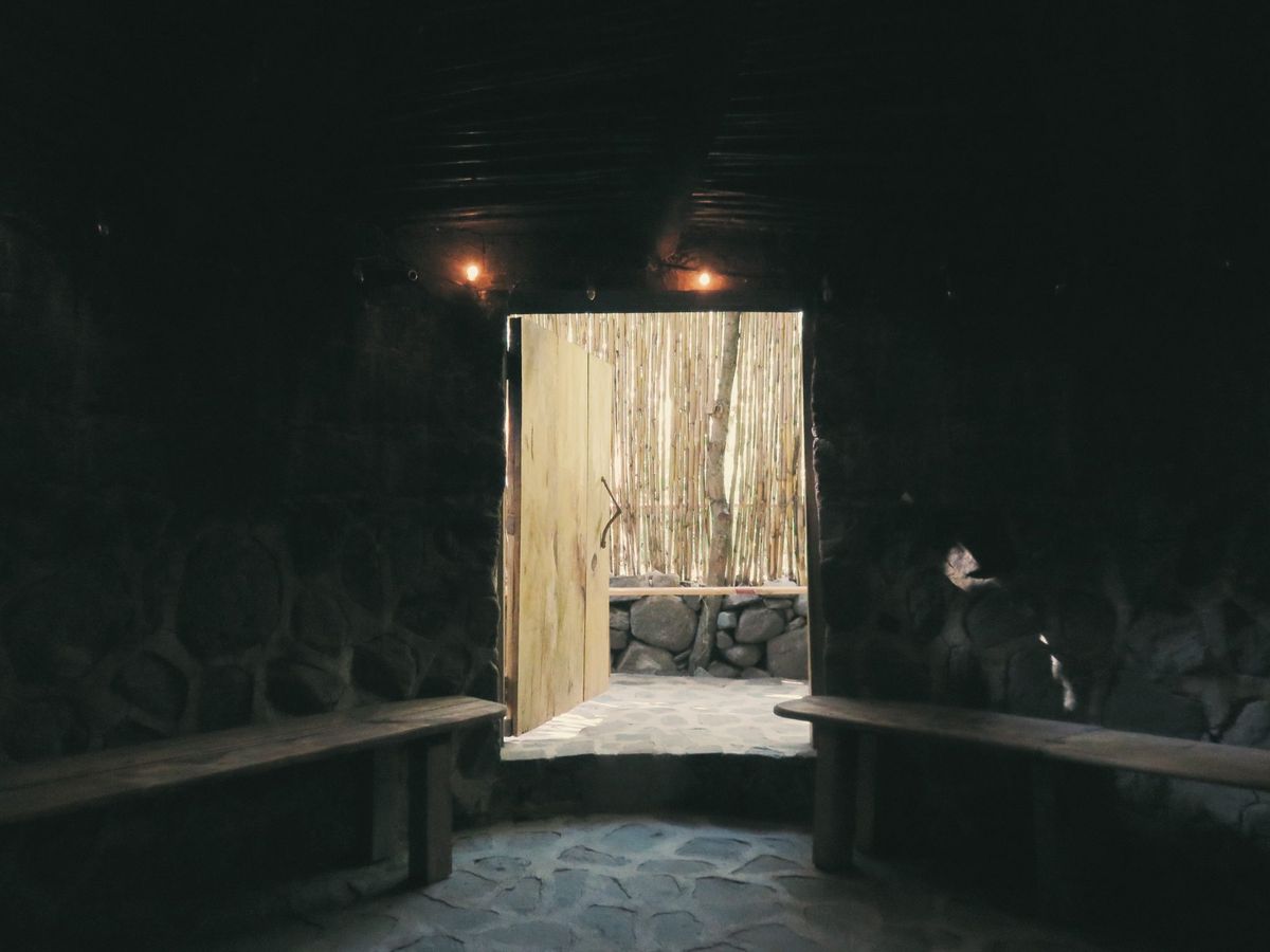The dark interior of a temazcal, with a low door and a bench.