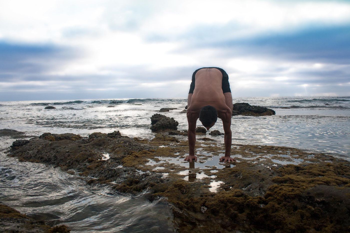 A wide-legged forward fold on the rocks by the sea.