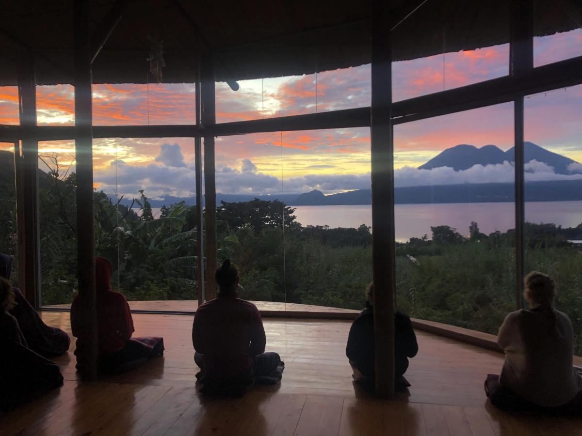 Students sitting in meditation, facing the lake at sunset.