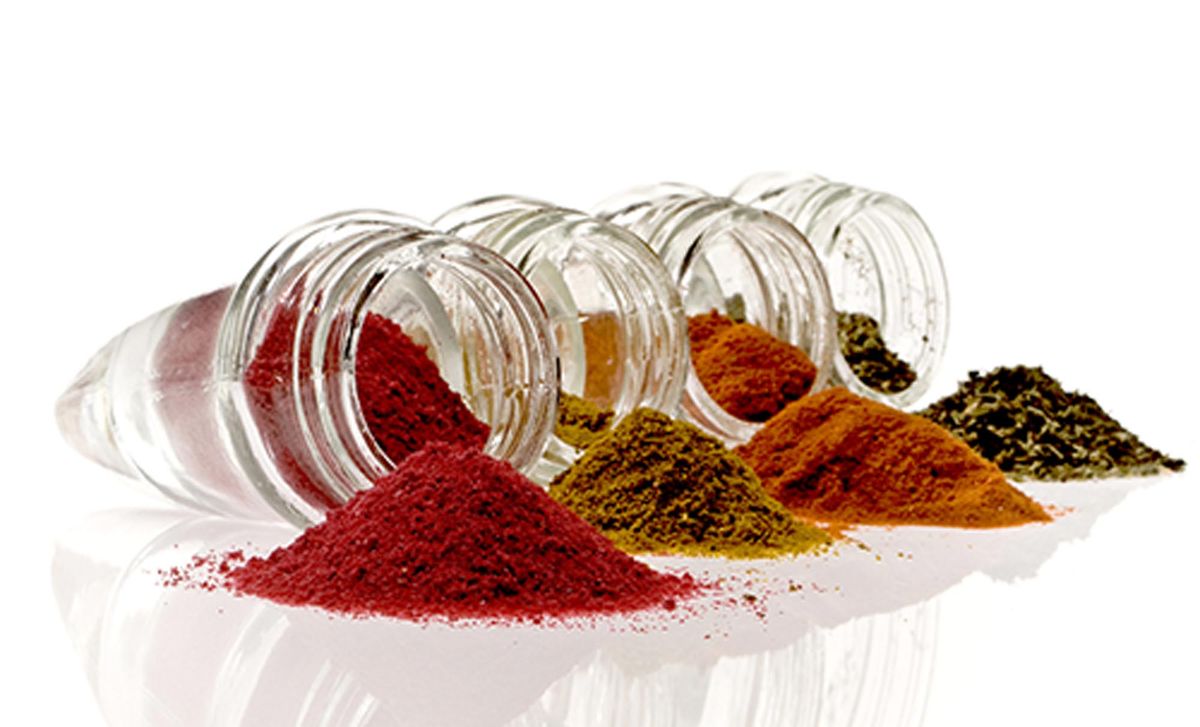 Jars of ground spices spilled on a white table.